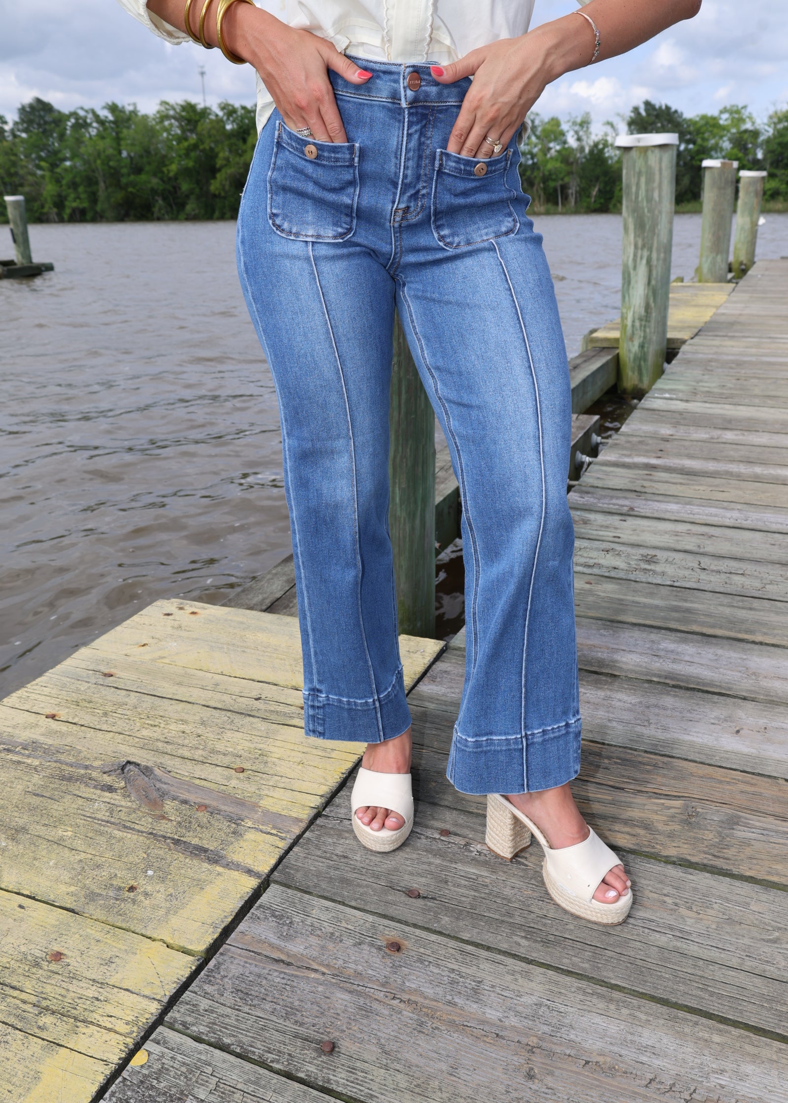 Person wearing blue jeans and white sandals on a wooden dock.