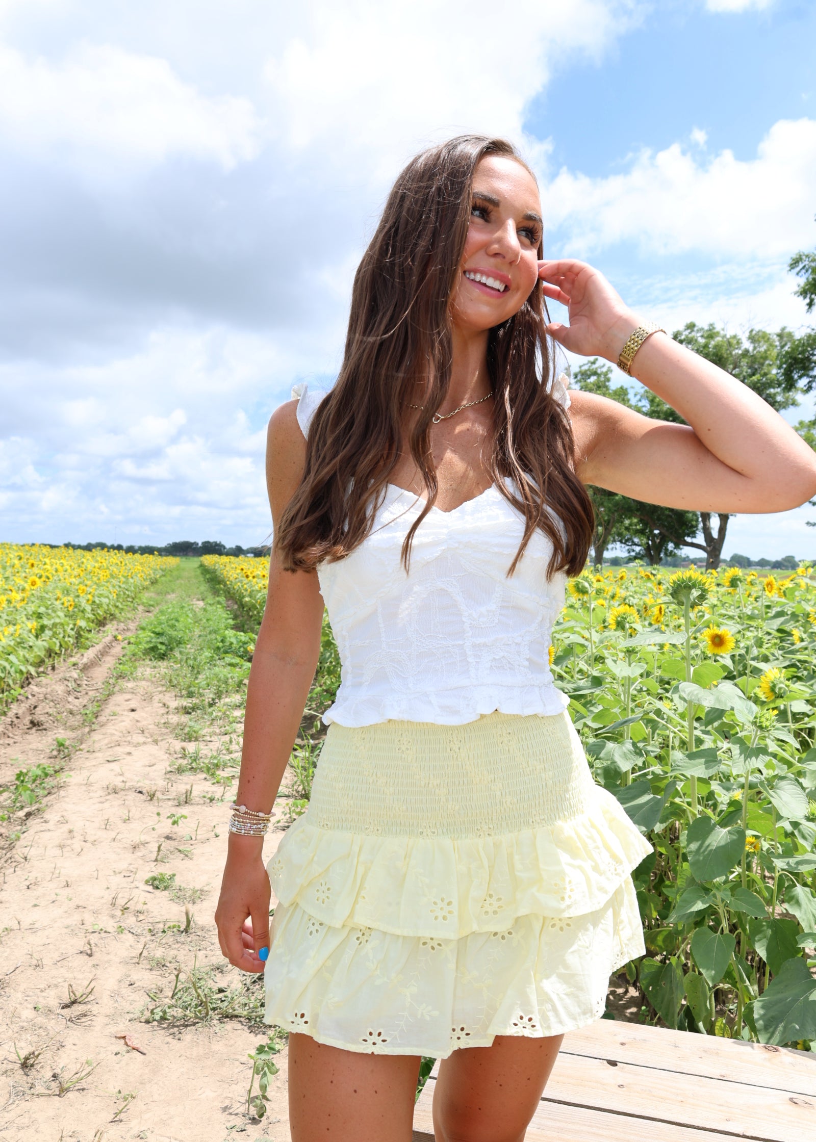 Woman in a white dress standing in a sunflower field with a blue sky.
