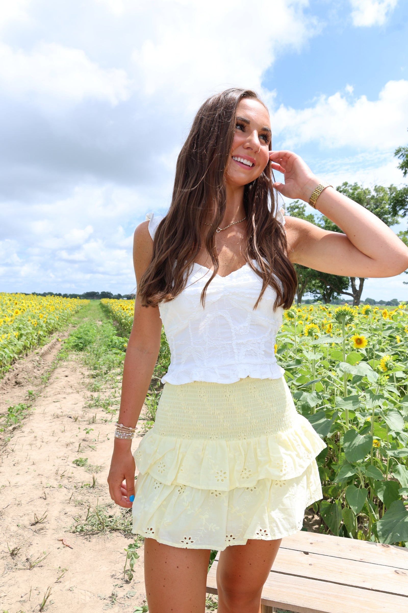 Woman in a white dress standing in a sunflower field with a blue sky.