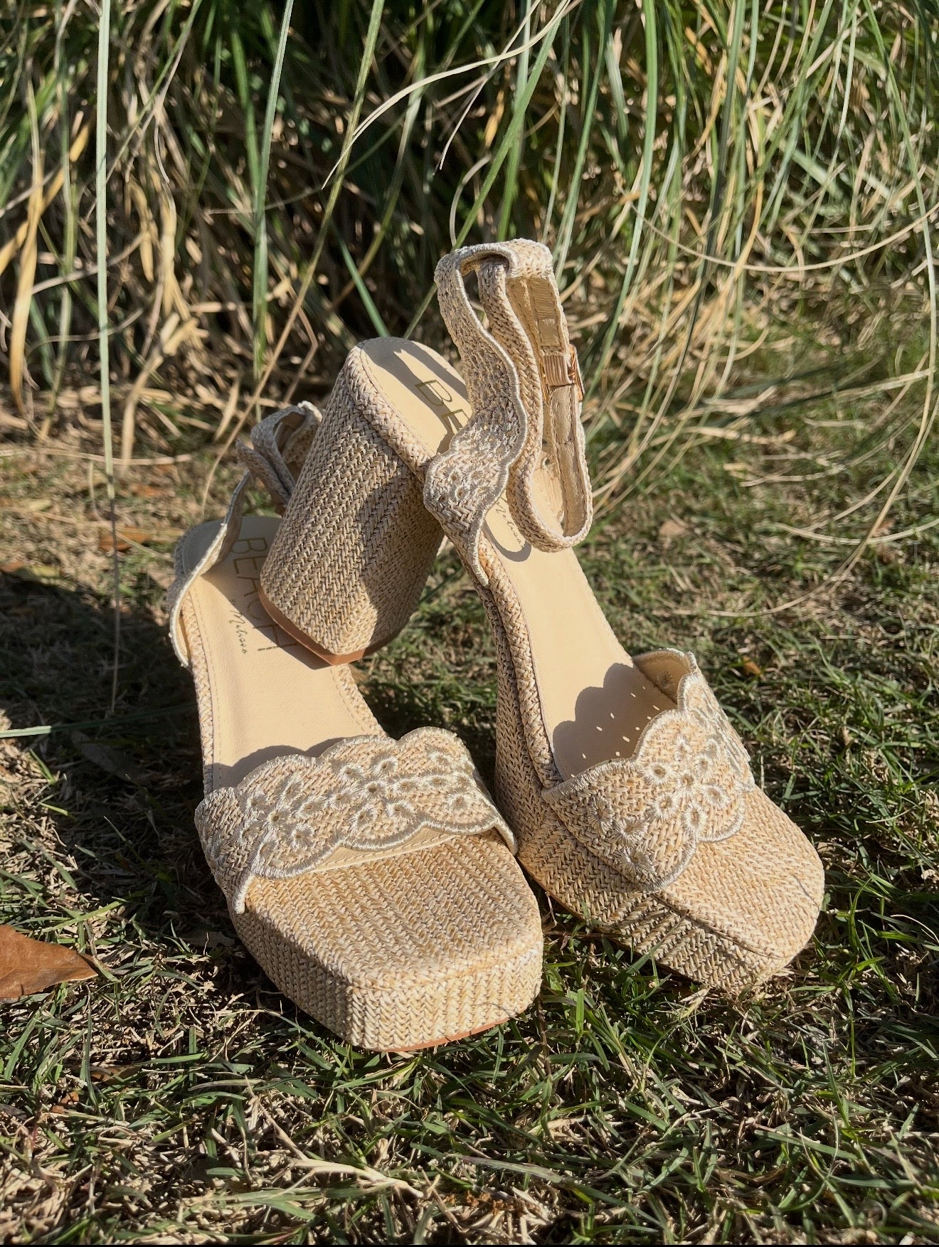 Pair of beige high-heeled shoes with decorative straps on grass