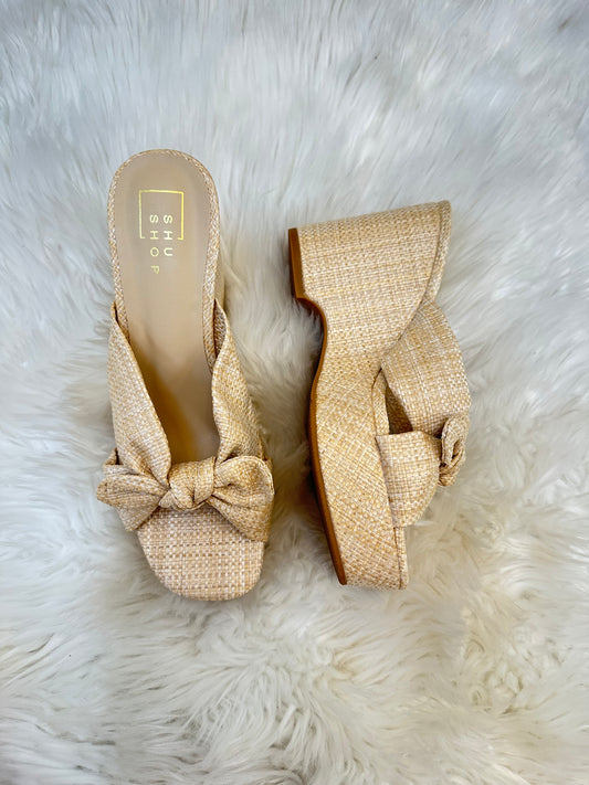 Pair of beige woven wedge sandals with a bow on a white fur background