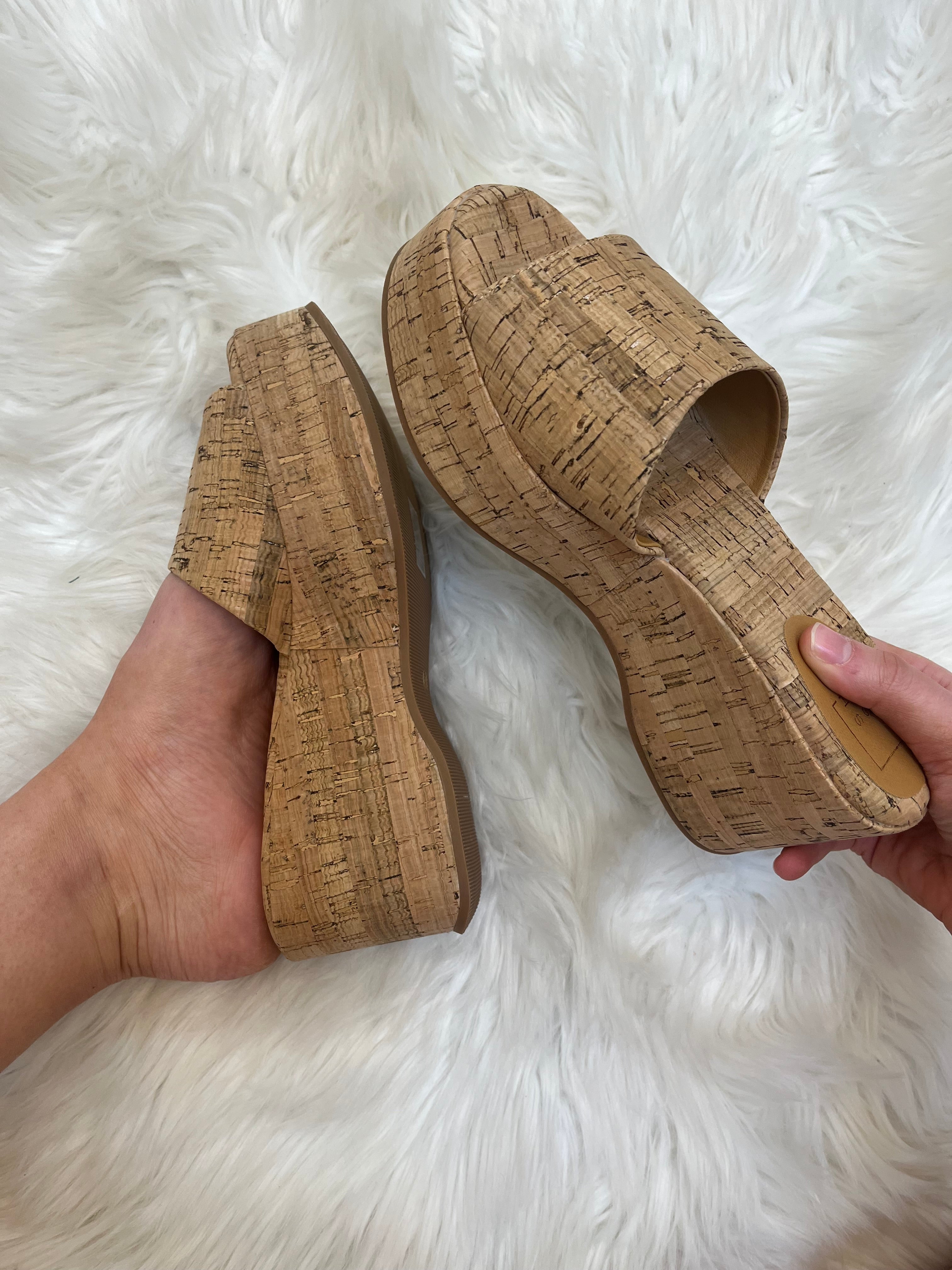 Pair of cork wedge sandals held by a hand on a white fluffy surface