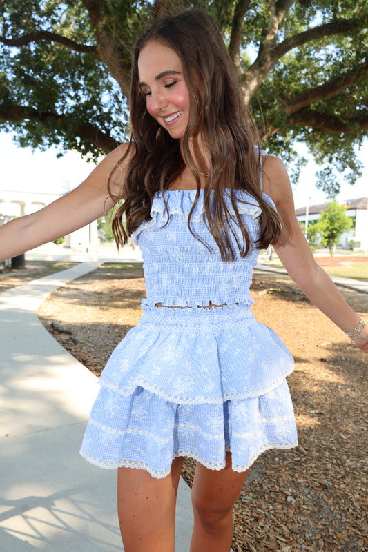 Woman wearing a light blue dress with ruffled sleeves and skirt, standing outdoors.