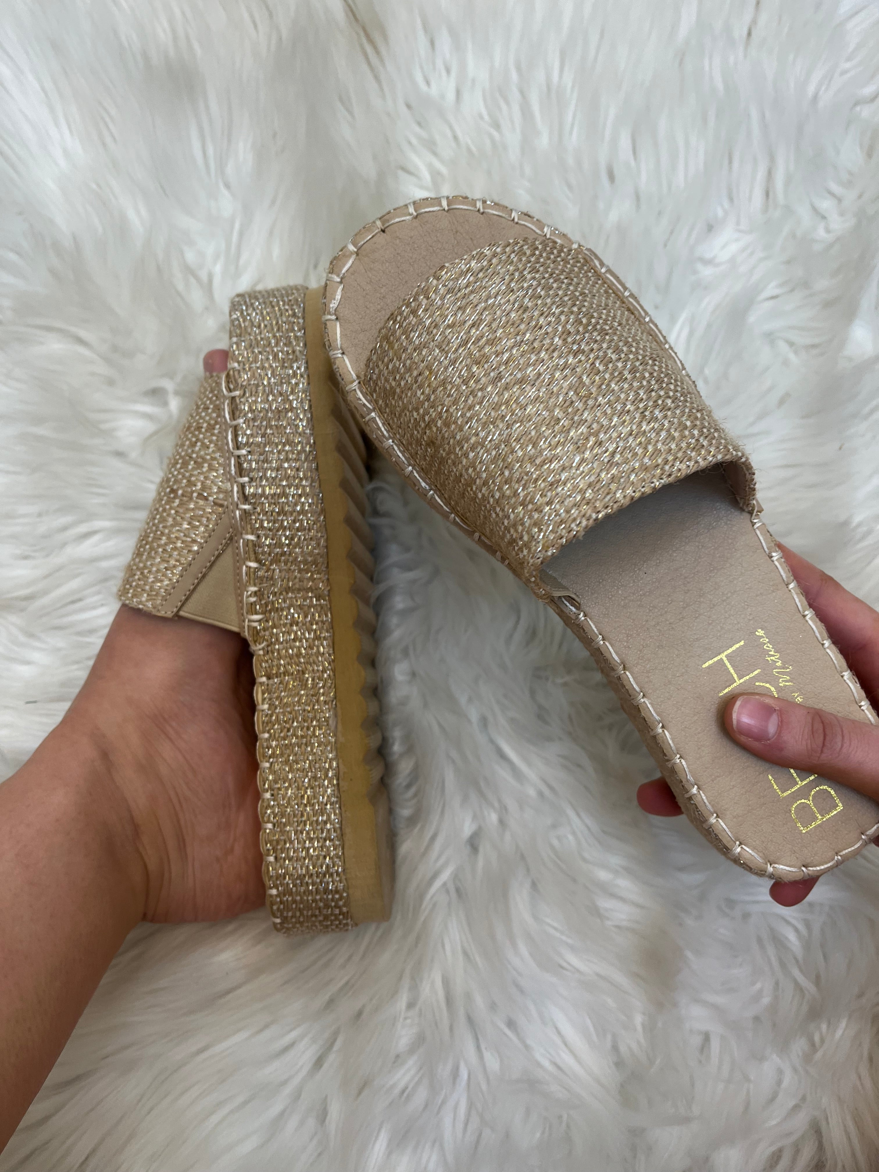 Beige espadrille sandals held by a hand on a white fluffy surface