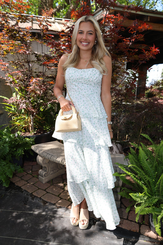 Woman in a light blue dress holding a beige clutch in a garden setting