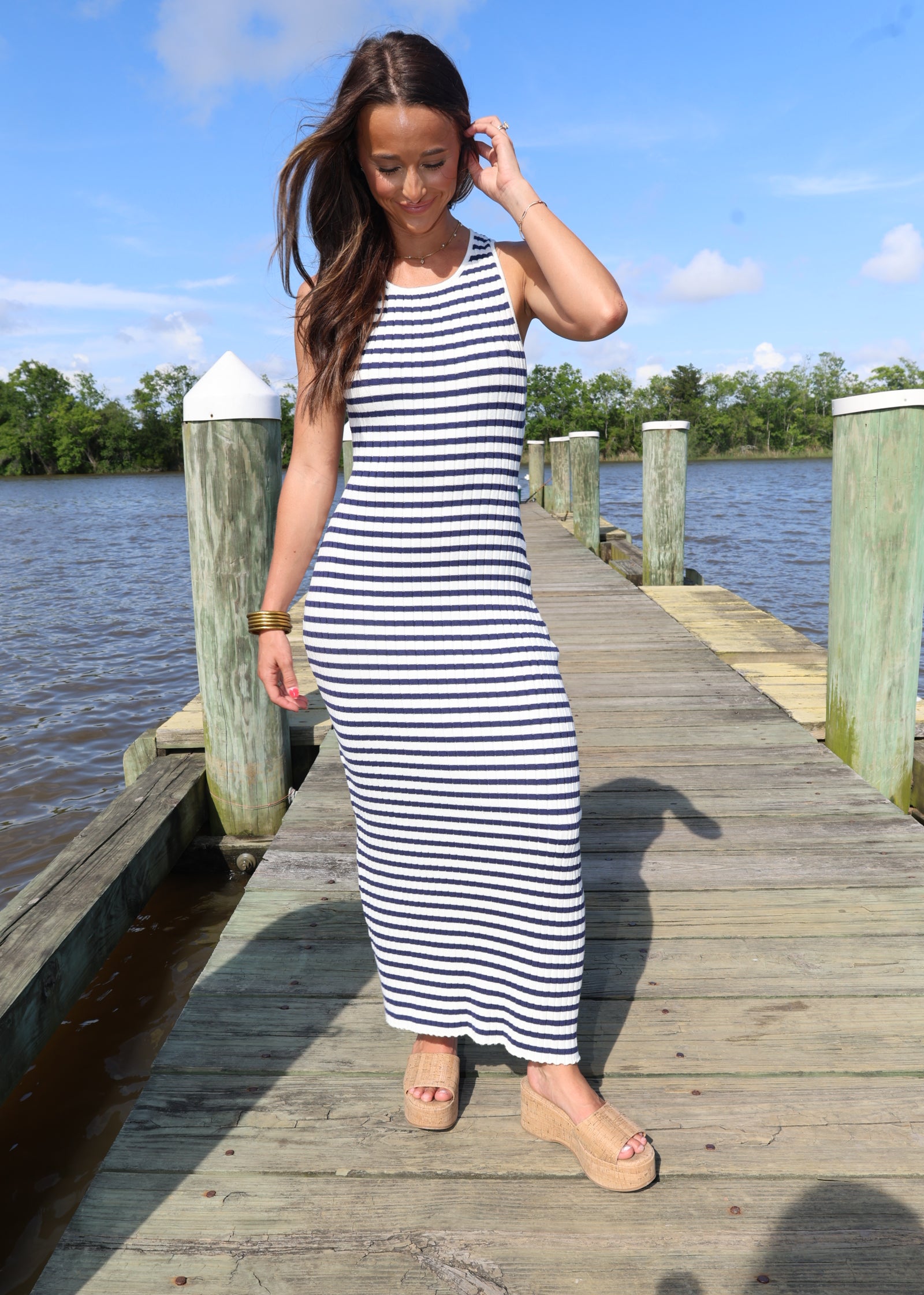 Woman in a striped dress standing on a wooden dock by a body of water.