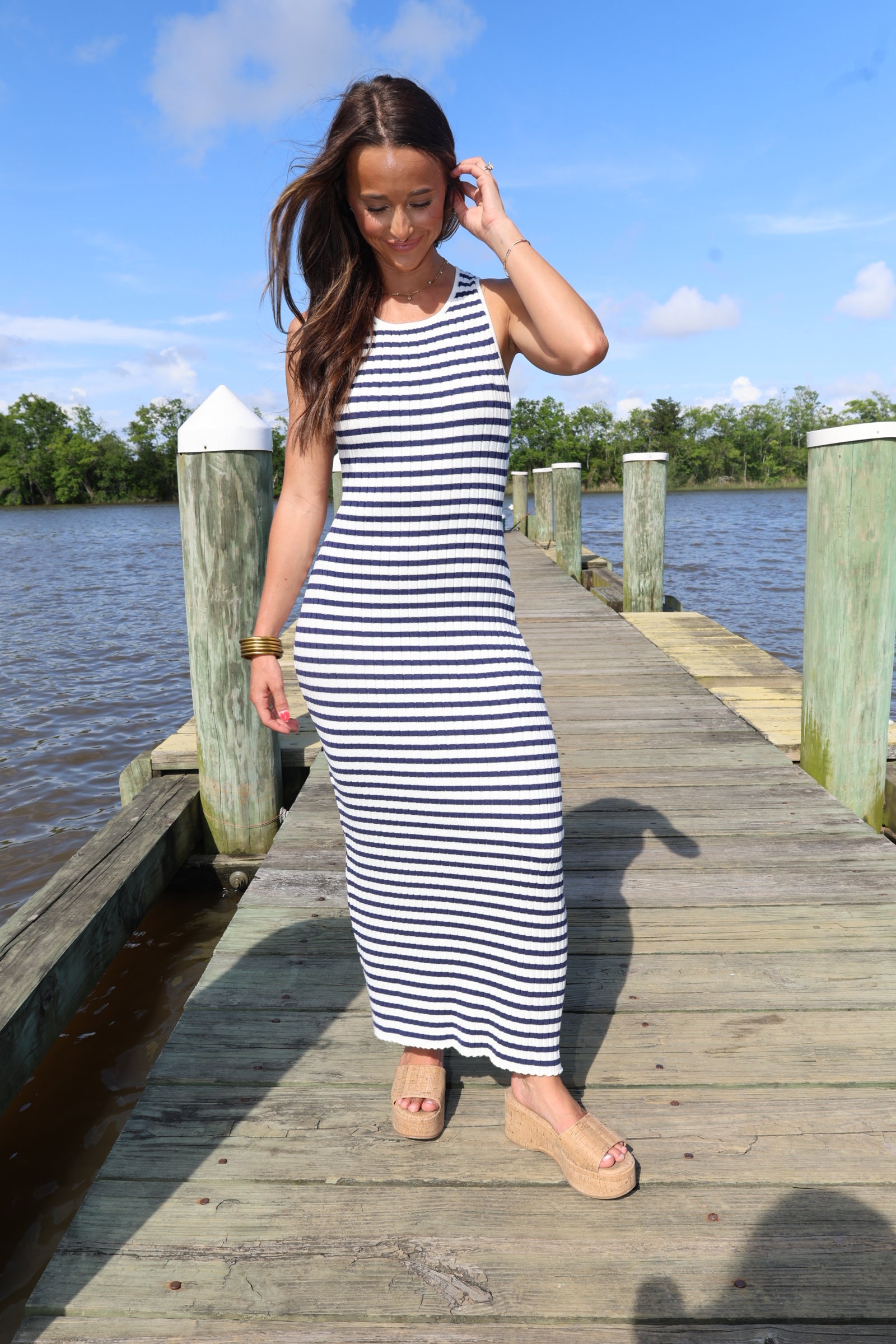 Woman in a striped dress standing on a wooden dock by a body of water.
