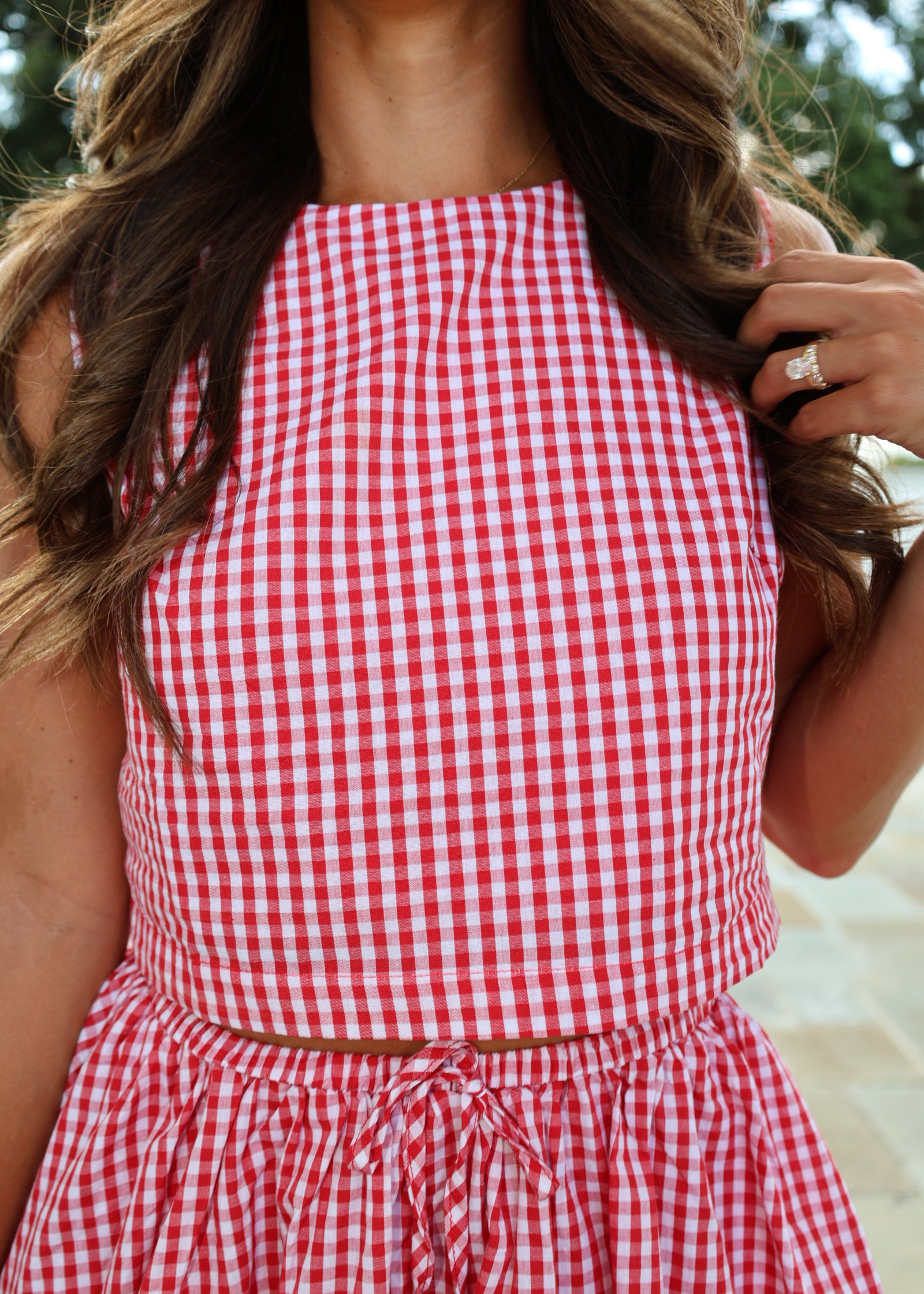 A close-up of a person wearing a red and white gingham check dress, shown from a side profile with long brown hair.