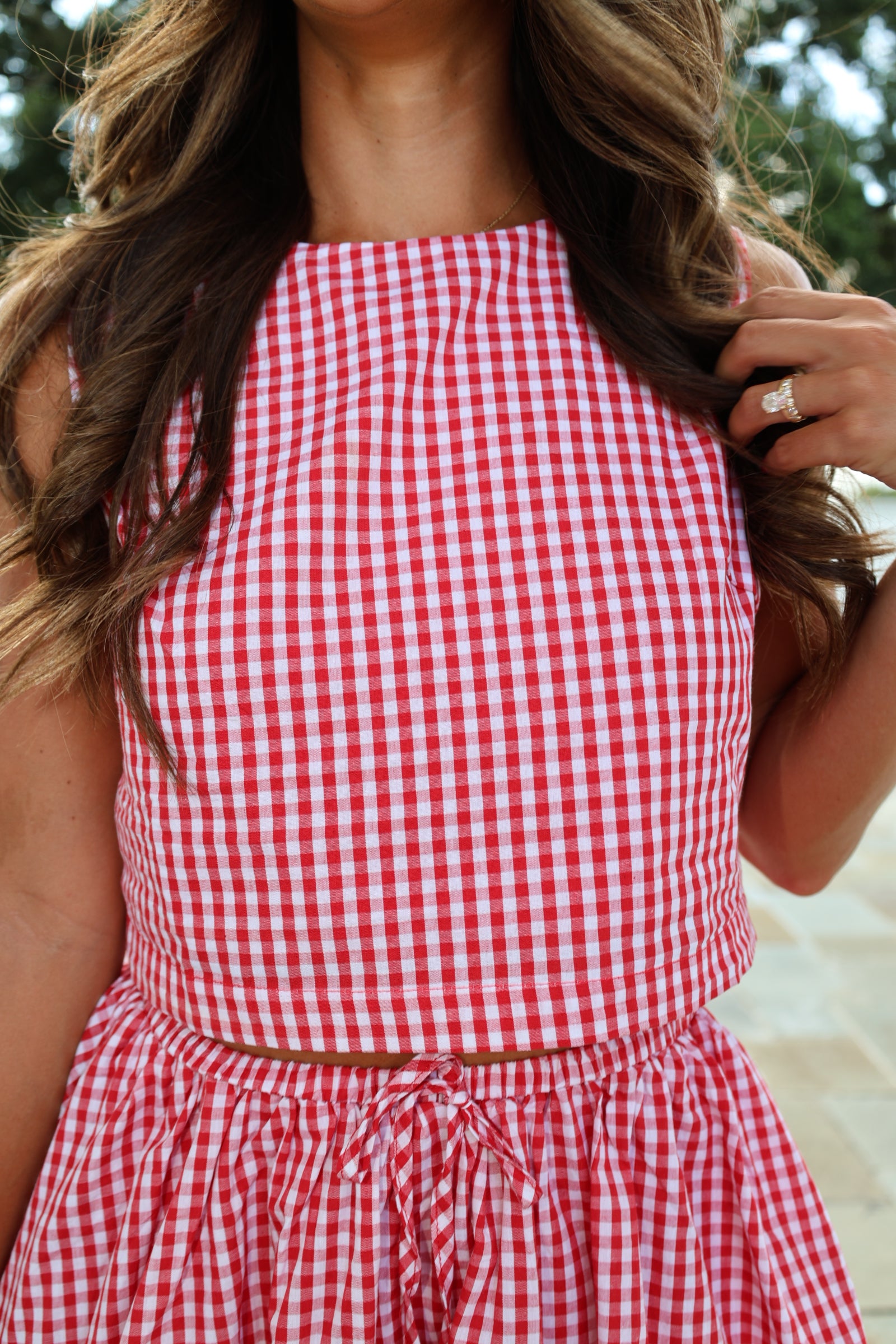 A close-up of a person wearing a red and white gingham check dress, shown from a side profile with long brown hair.
