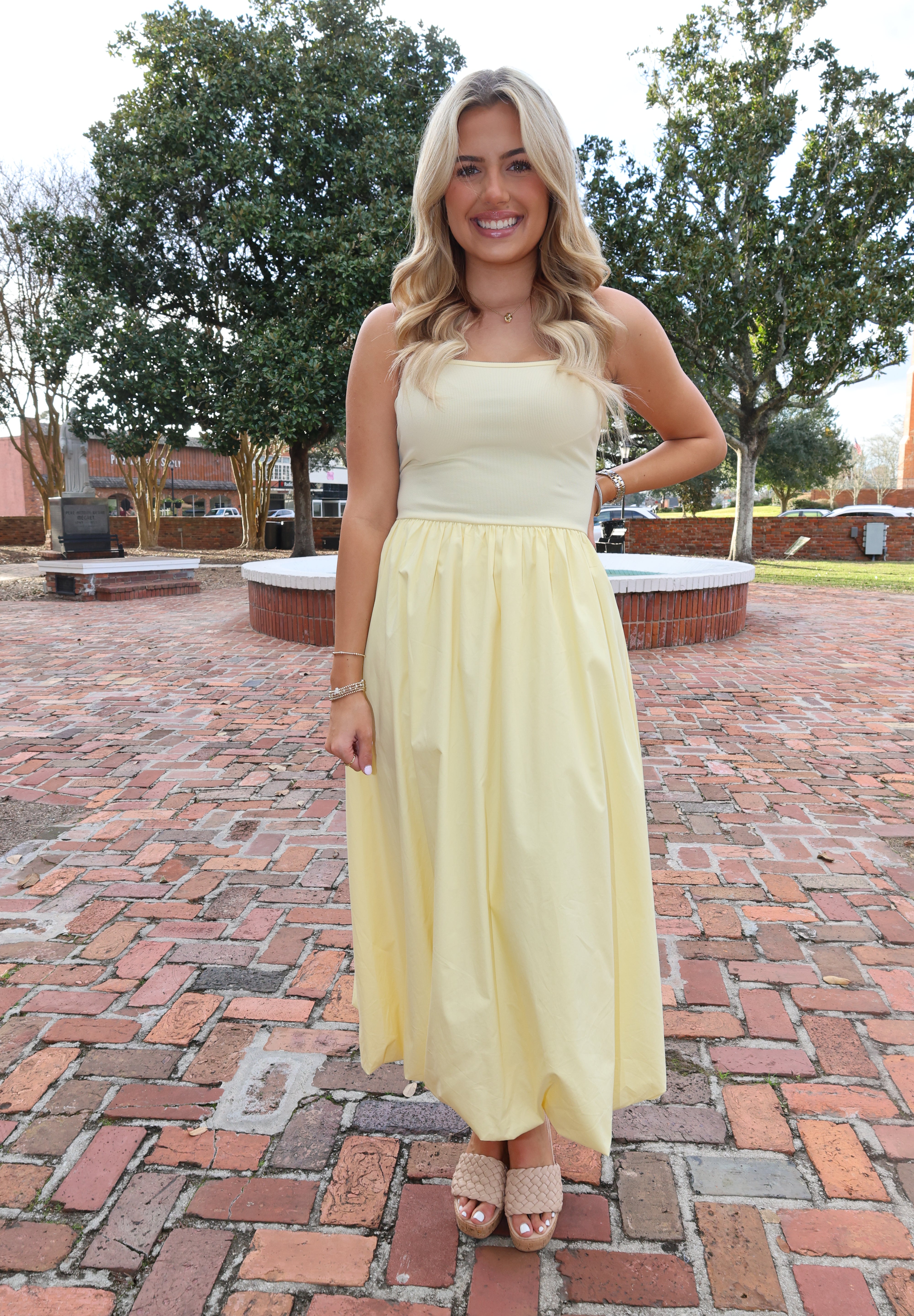 Woman in a yellow dress standing on a brick path with trees in the background