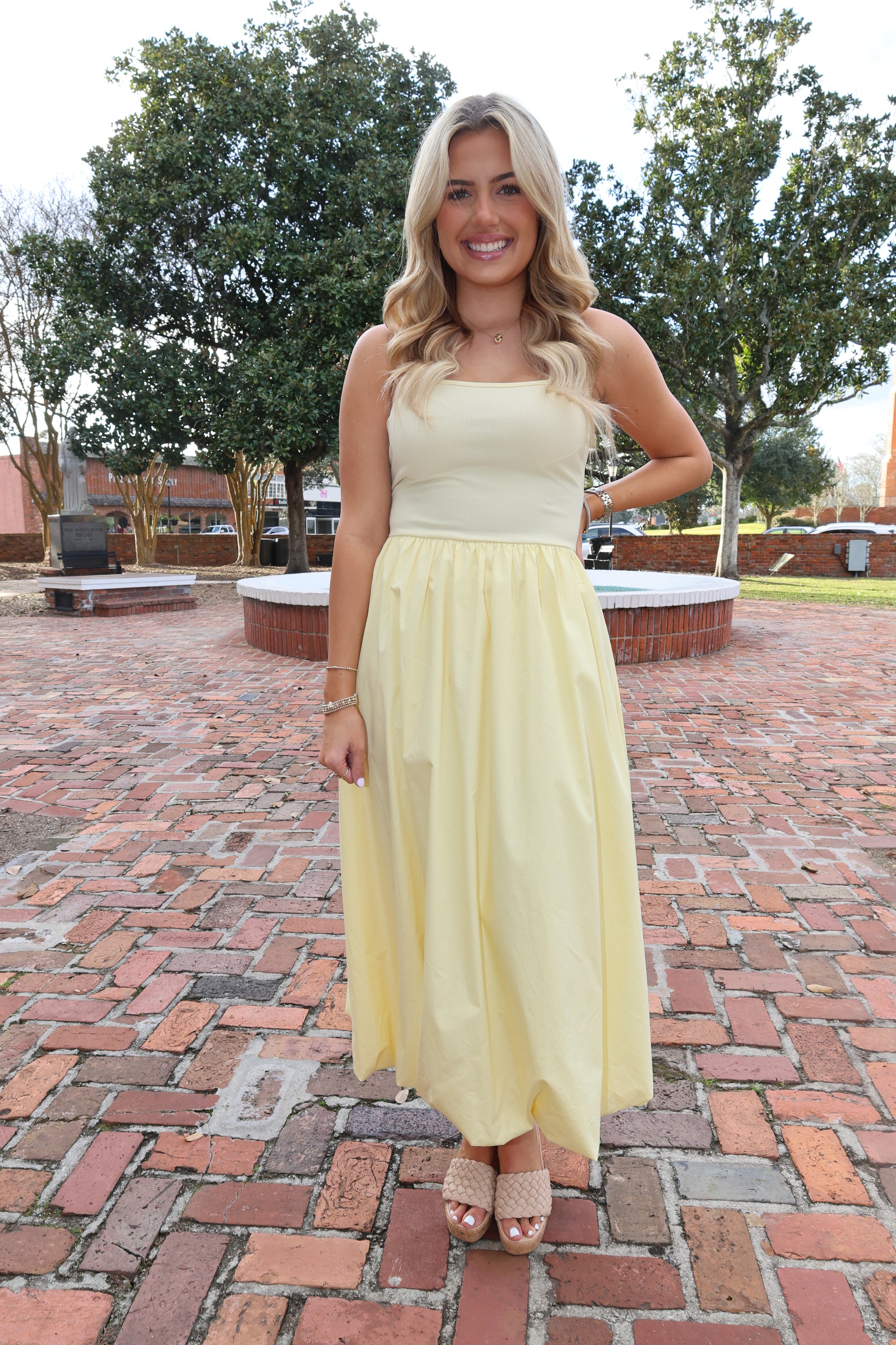 Woman in a yellow dress standing on a brick path with trees in the background