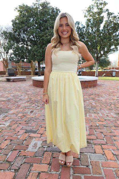 Woman in a yellow dress standing on a brick path with trees in the background