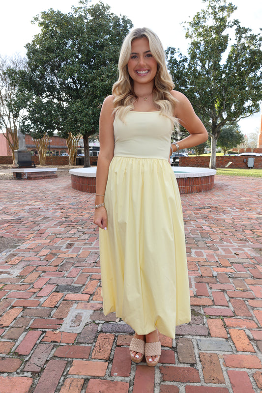 Woman in a yellow dress standing on a brick path with trees in the background