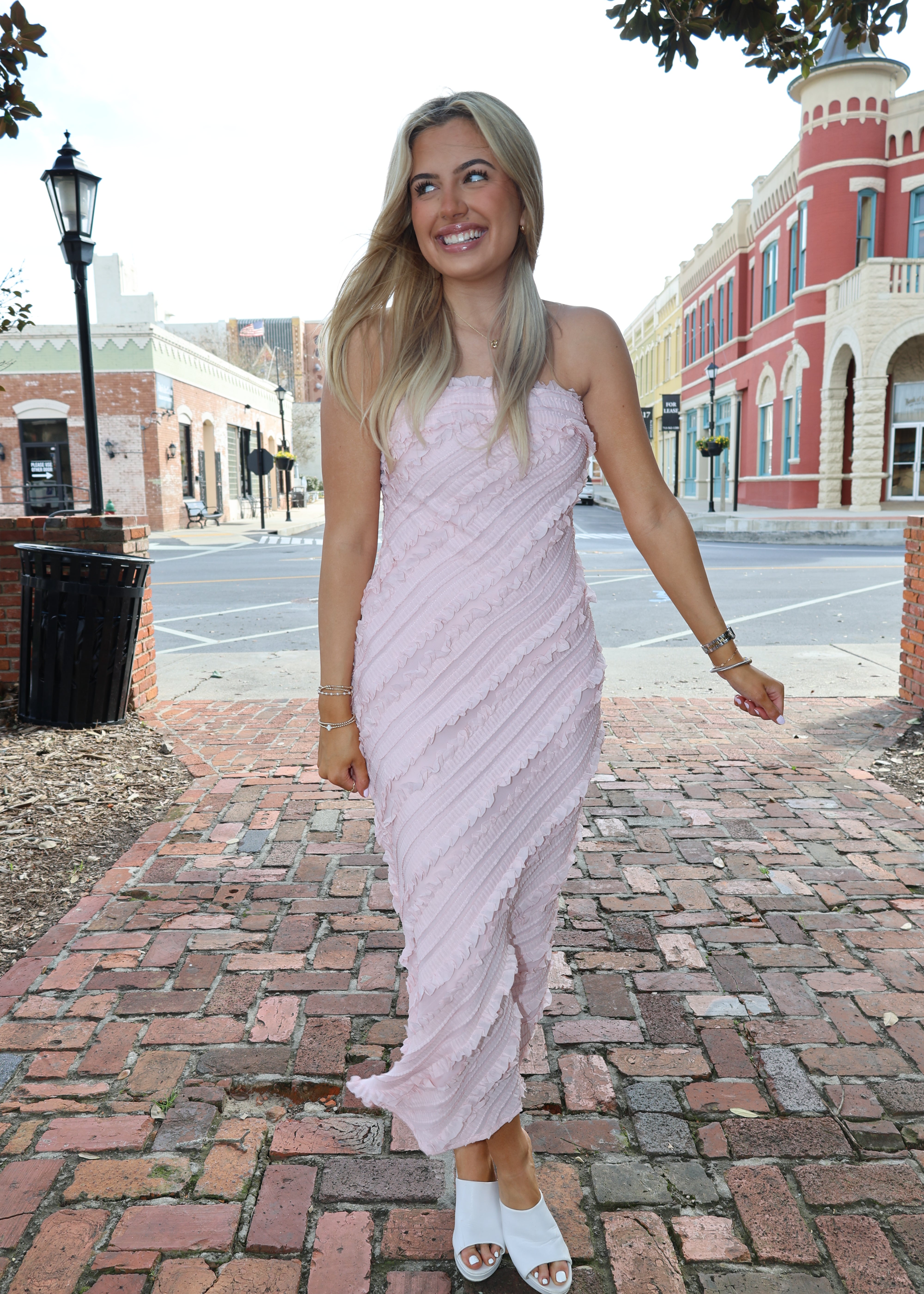 Woman in a white dress standing on a brick sidewalk with buildings in the background