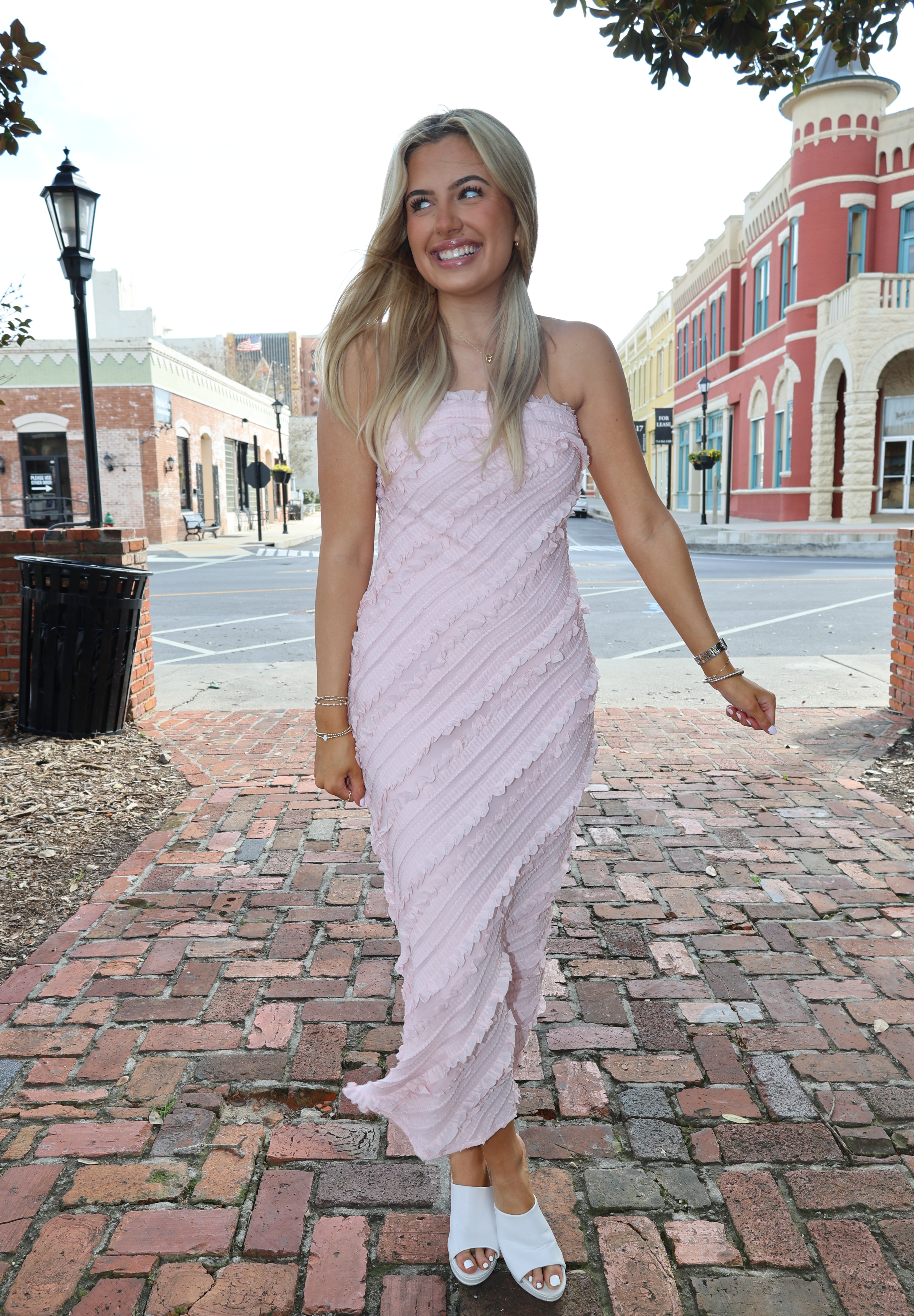 Woman in a white dress standing on a brick sidewalk with buildings in the background