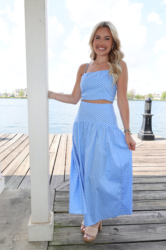 Woman in a blue polka dot dress standing on a wooden deck with a clear sky background