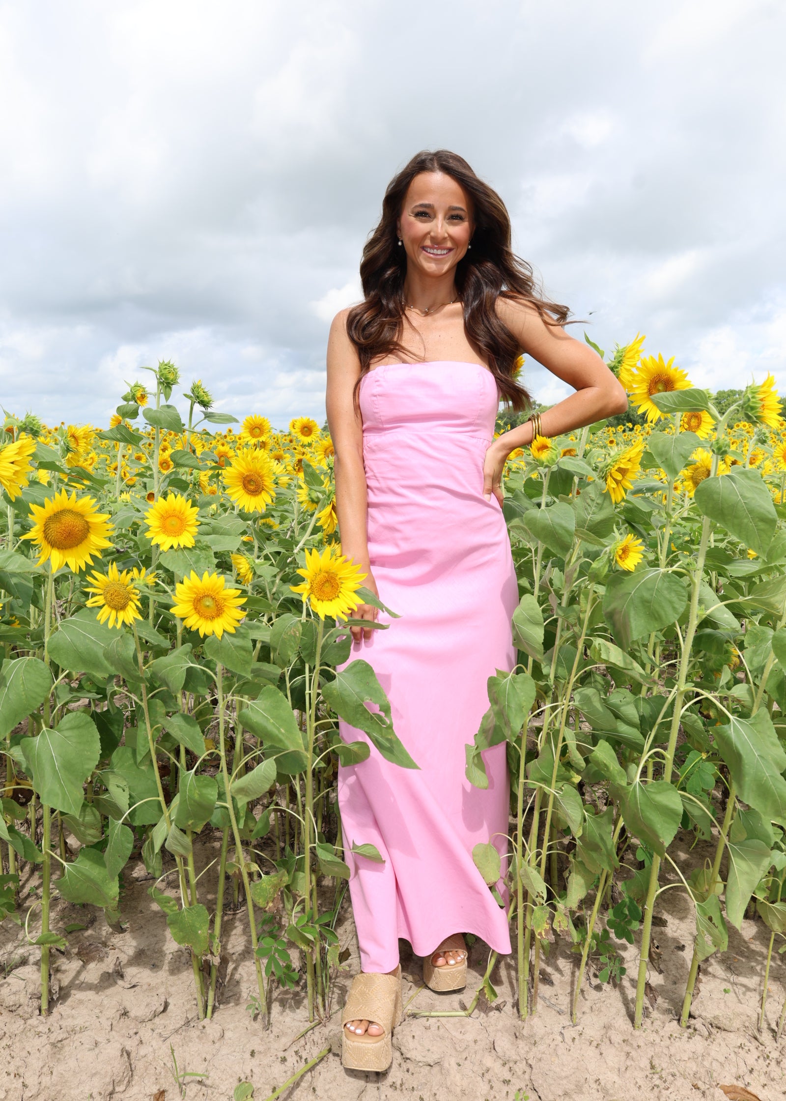 Woman in a pink dress lying on the sand with sunflowers around her