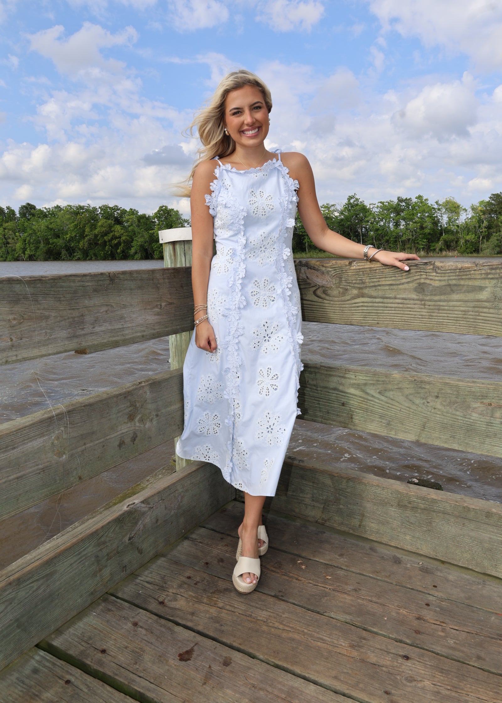 Woman in a white dress standing on wooden planks with a blue sky and clouds in the background