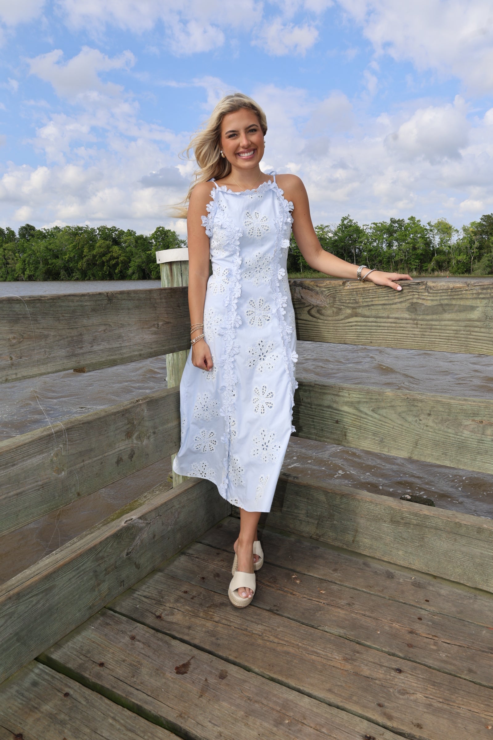 Woman in a white dress standing on wooden planks with a blue sky and clouds in the background