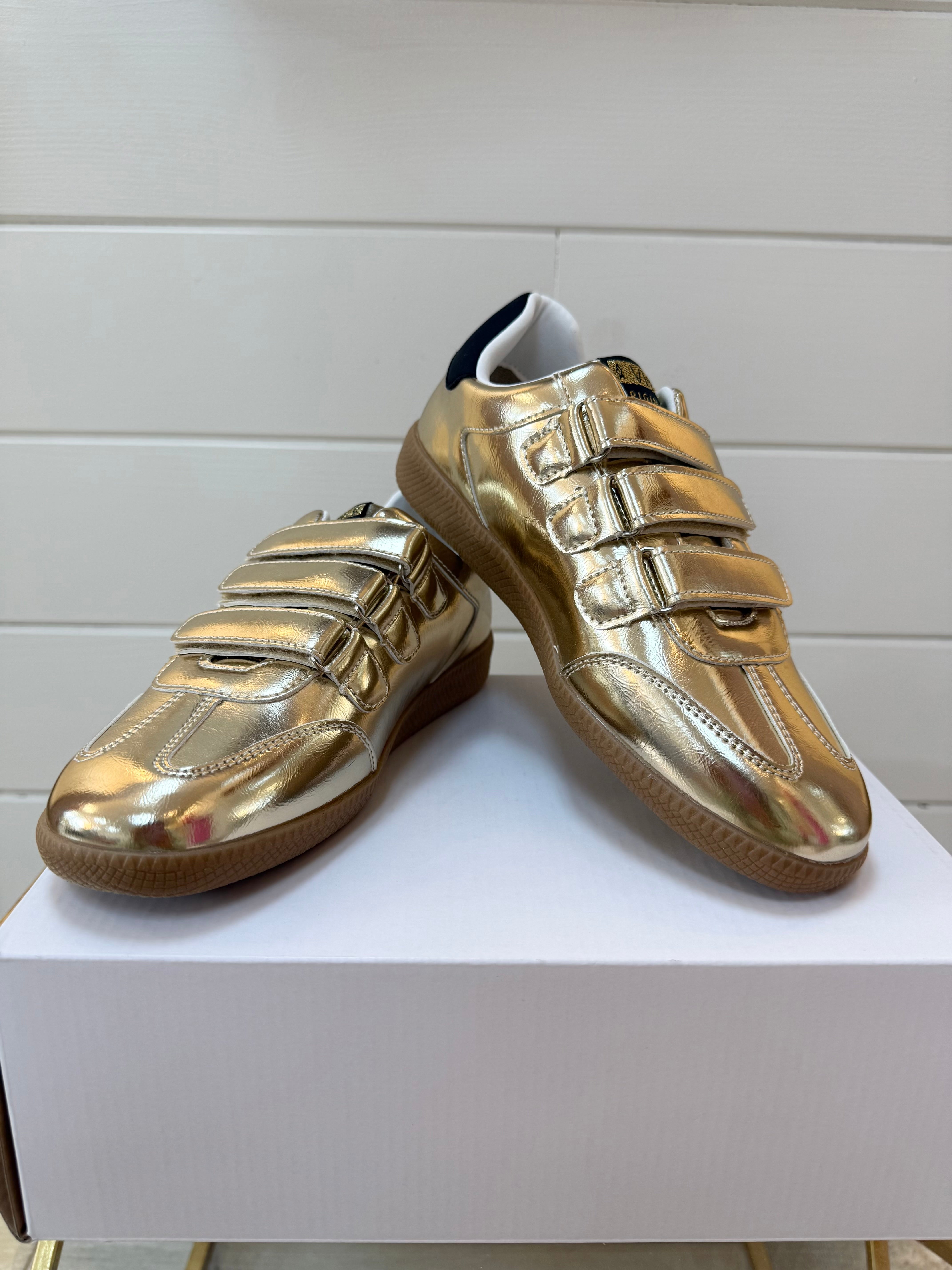 Pair of gold shoes on a white box with a white background