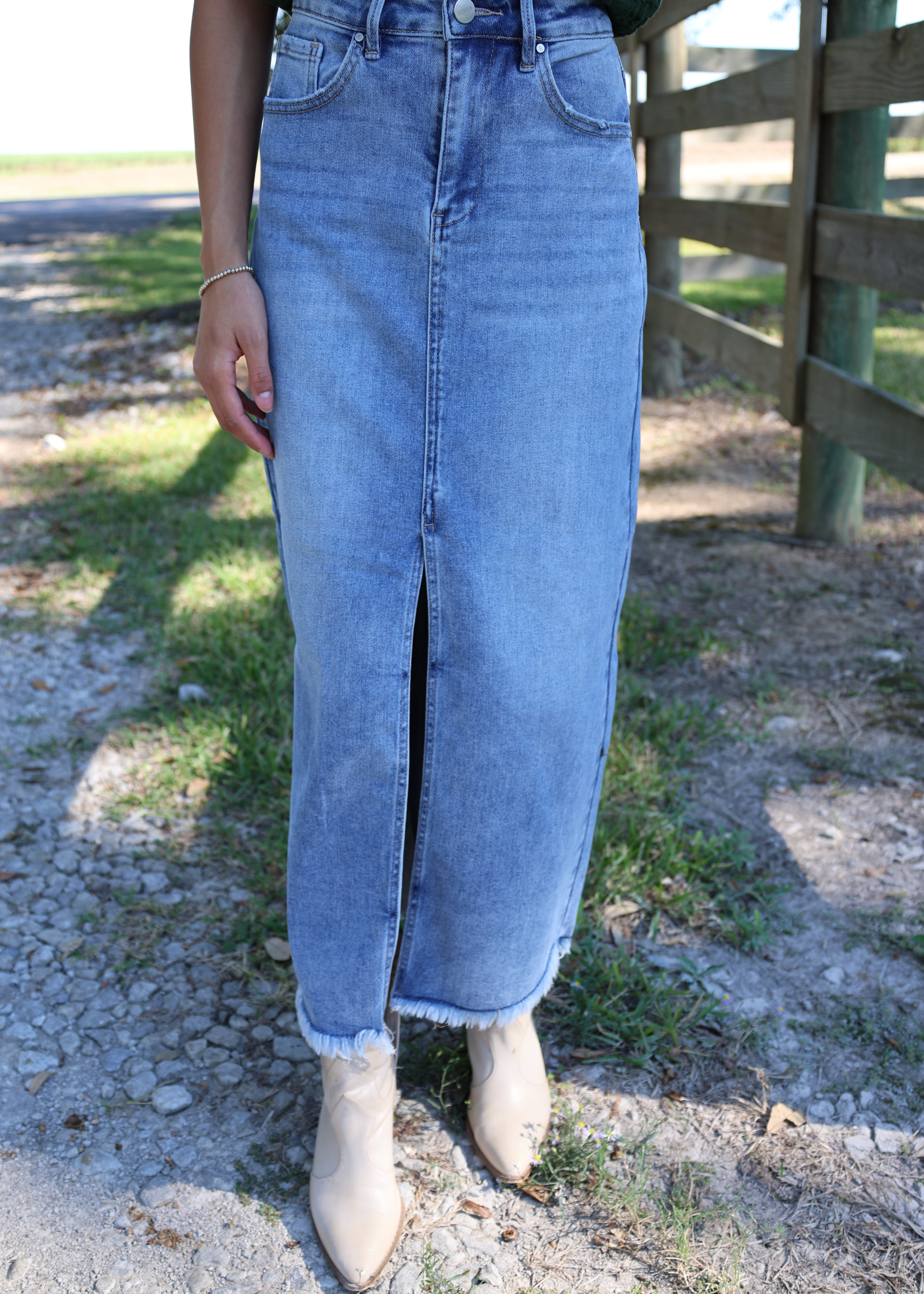 Person wearing light blue jeans standing on a stone path with grass and water in the background