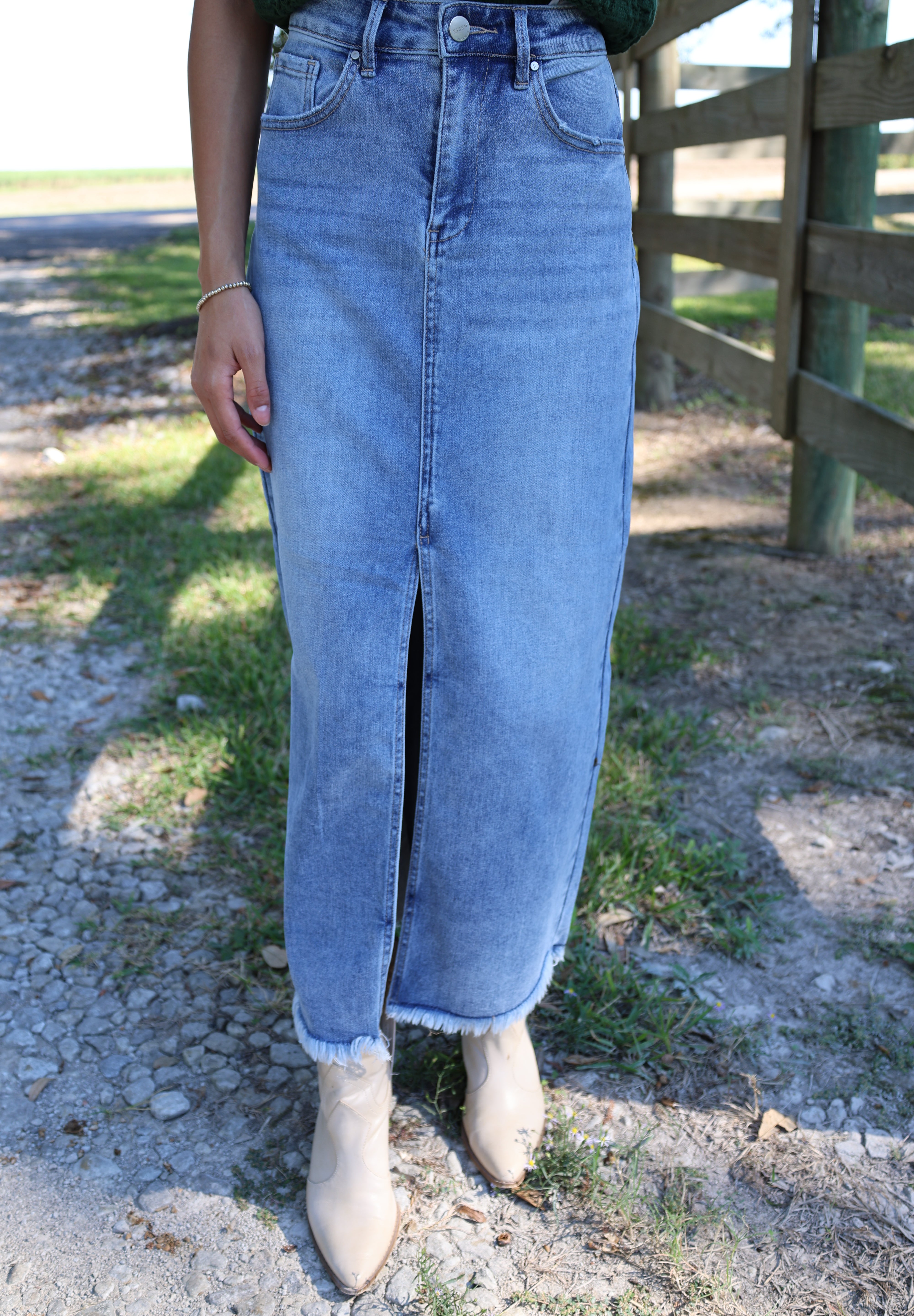 Person wearing light blue jeans standing on a stone path with grass and water in the background