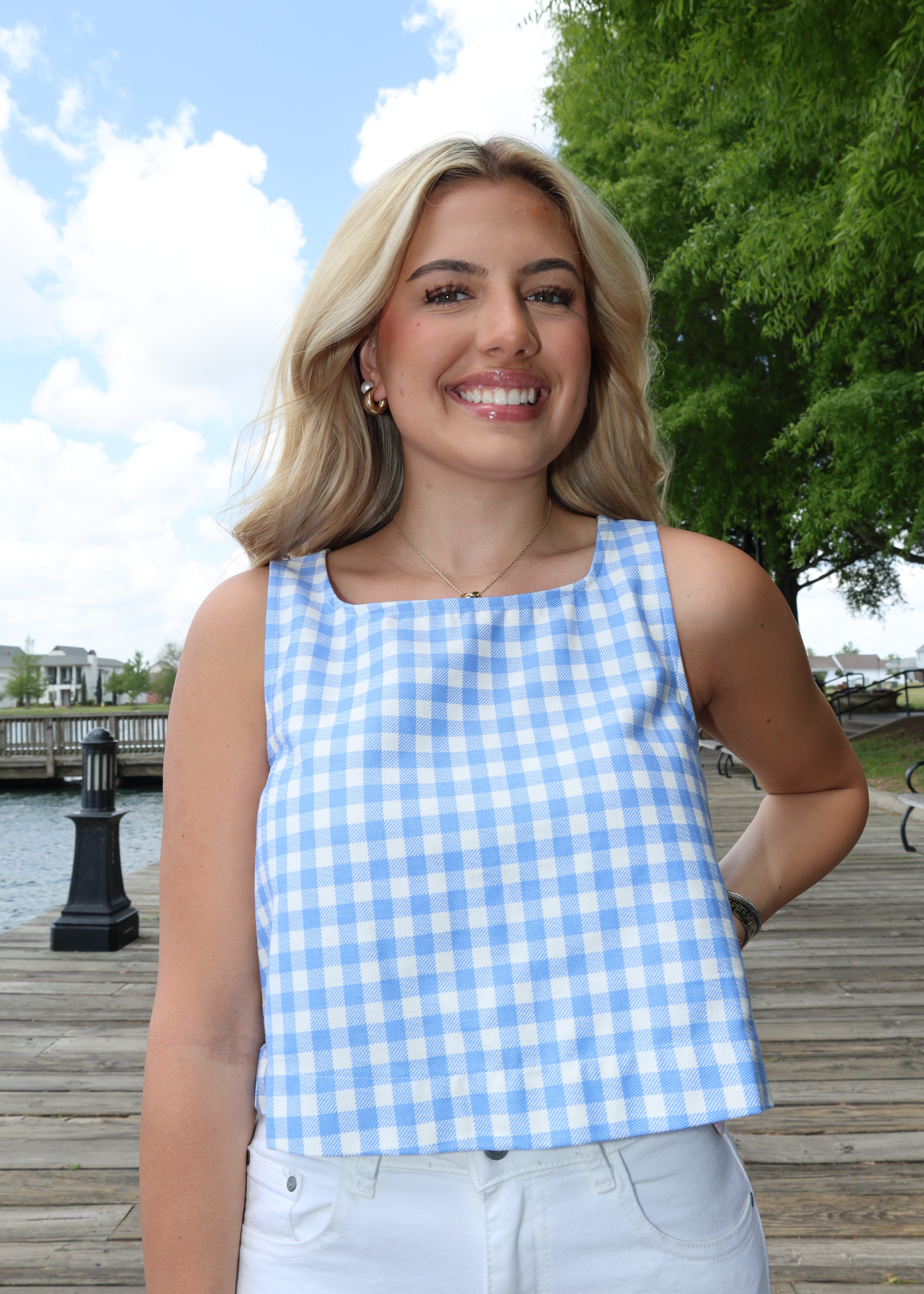 Woman wearing a blue and white checkered dress standing outdoors with trees and a clear sky in the background.