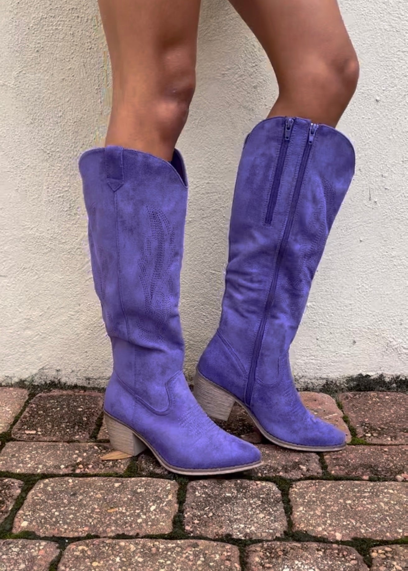 Purple knee-high boots worn on a stone pavement with a light-colored wall background