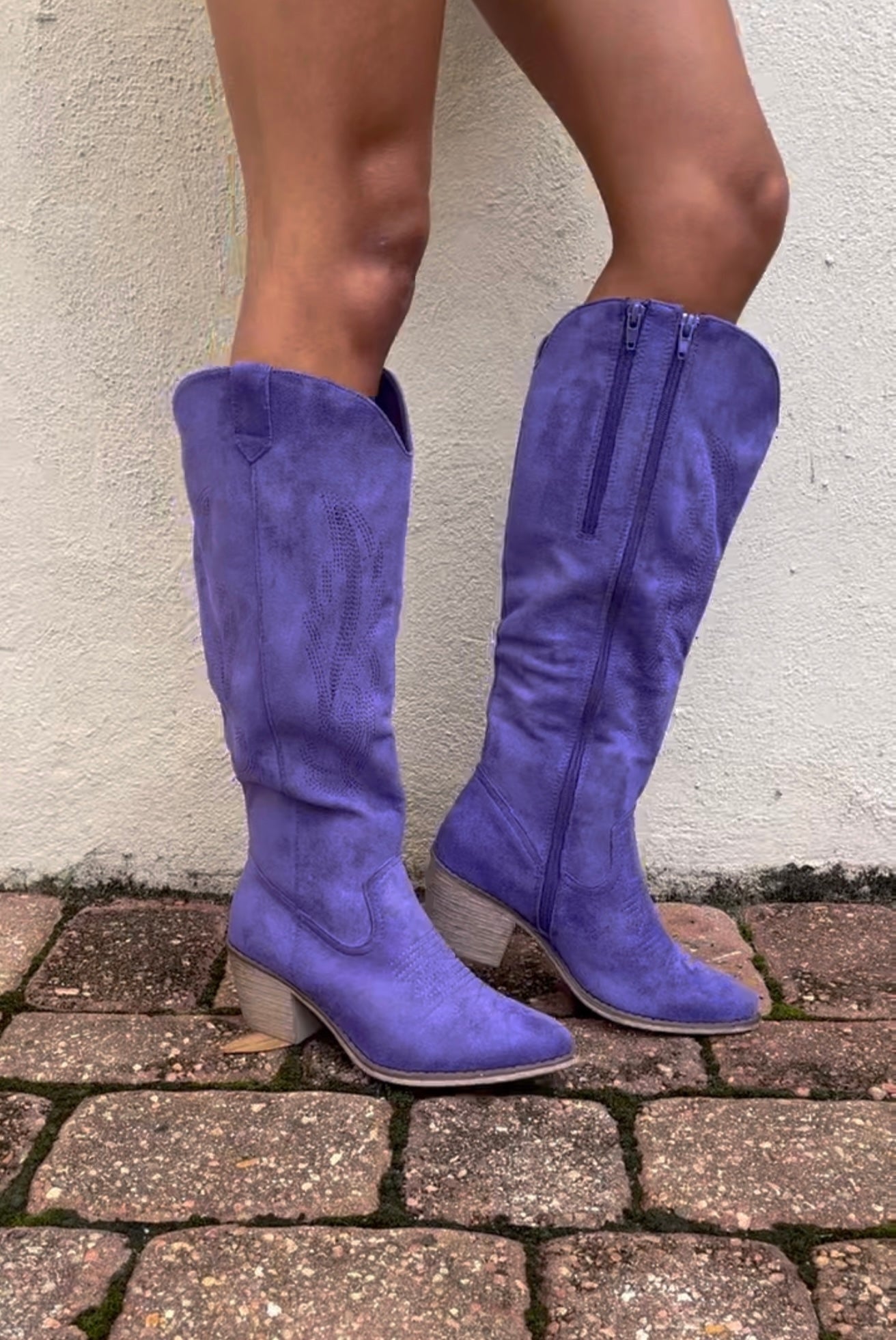 Purple knee-high boots worn on a stone pavement with a light-colored wall background
