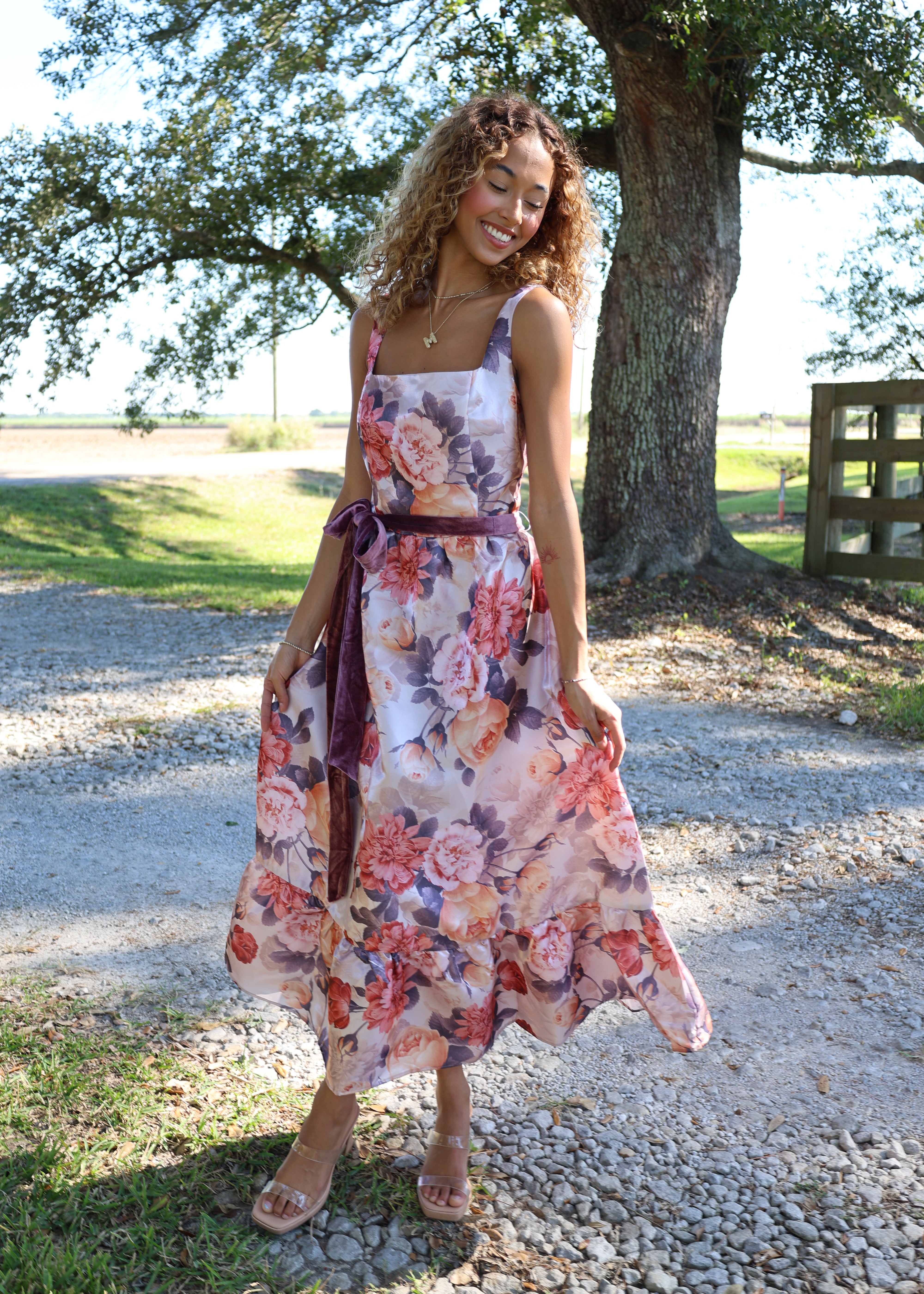 Woman in a floral dress standing outdoors near a tree