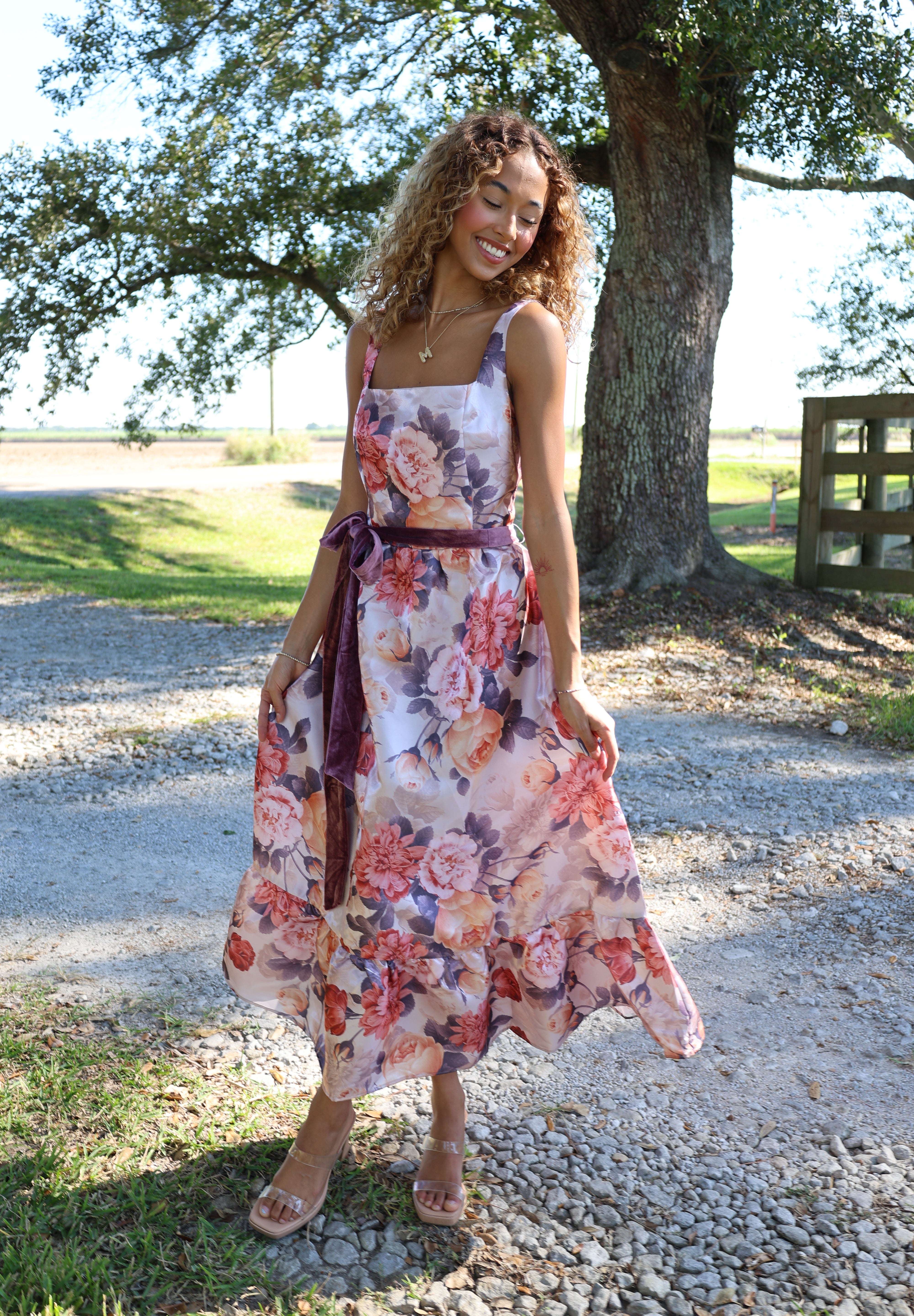 Woman in a floral dress standing outdoors near a tree