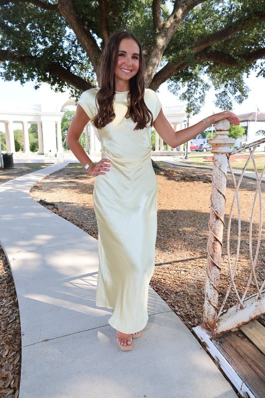 Woman in a white dress standing on a sidewalk with trees and a car in the background