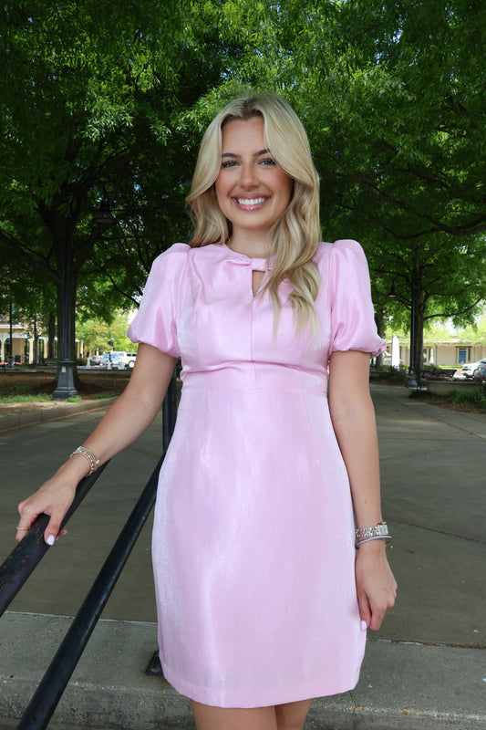 Woman in a pink dress standing outdoors with trees in the background