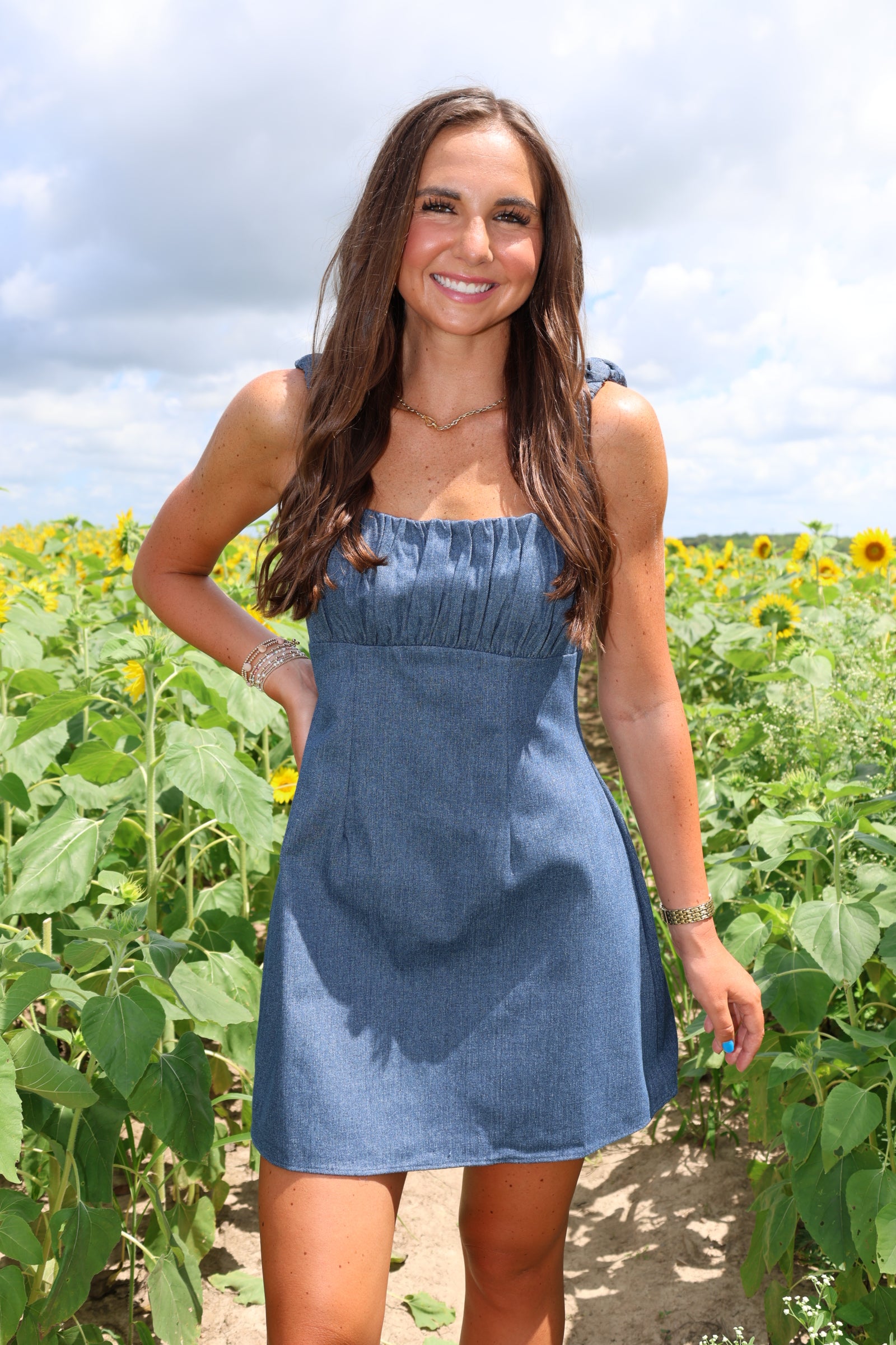 Woman in a blue dress standing in a field with greenery and sunflowers.