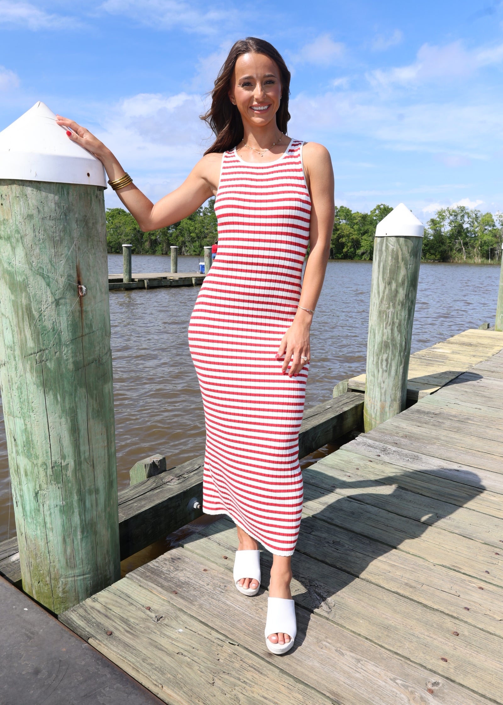 Woman in a red and white striped dress standing on a wooden dock by a body of water.