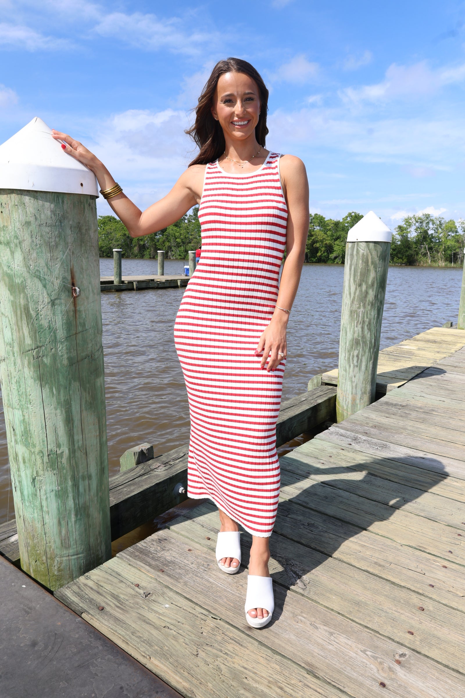 Woman in a red and white striped dress standing on a wooden dock by a body of water.