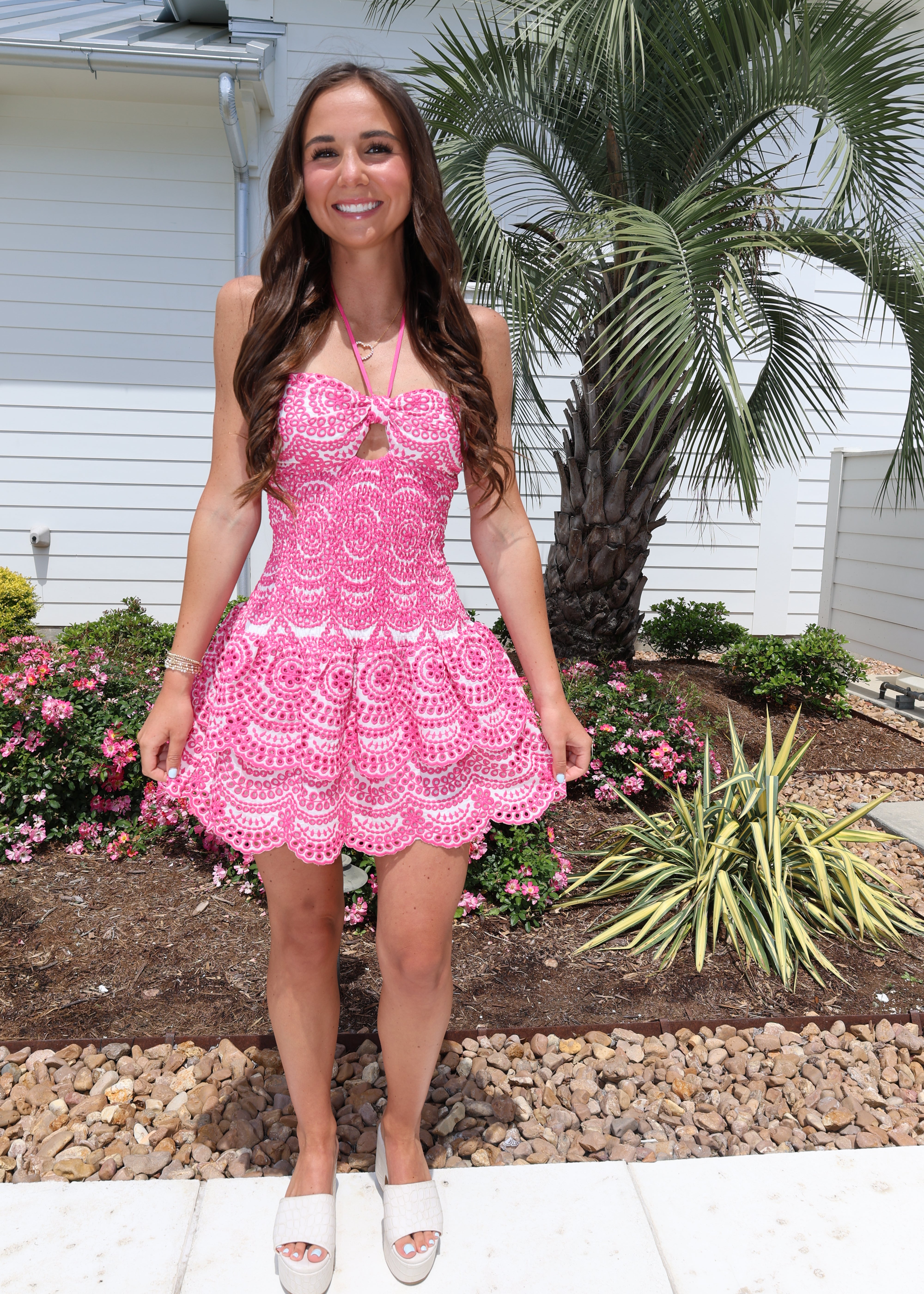 Woman in a pink dress standing outdoors with plants and a house in the background