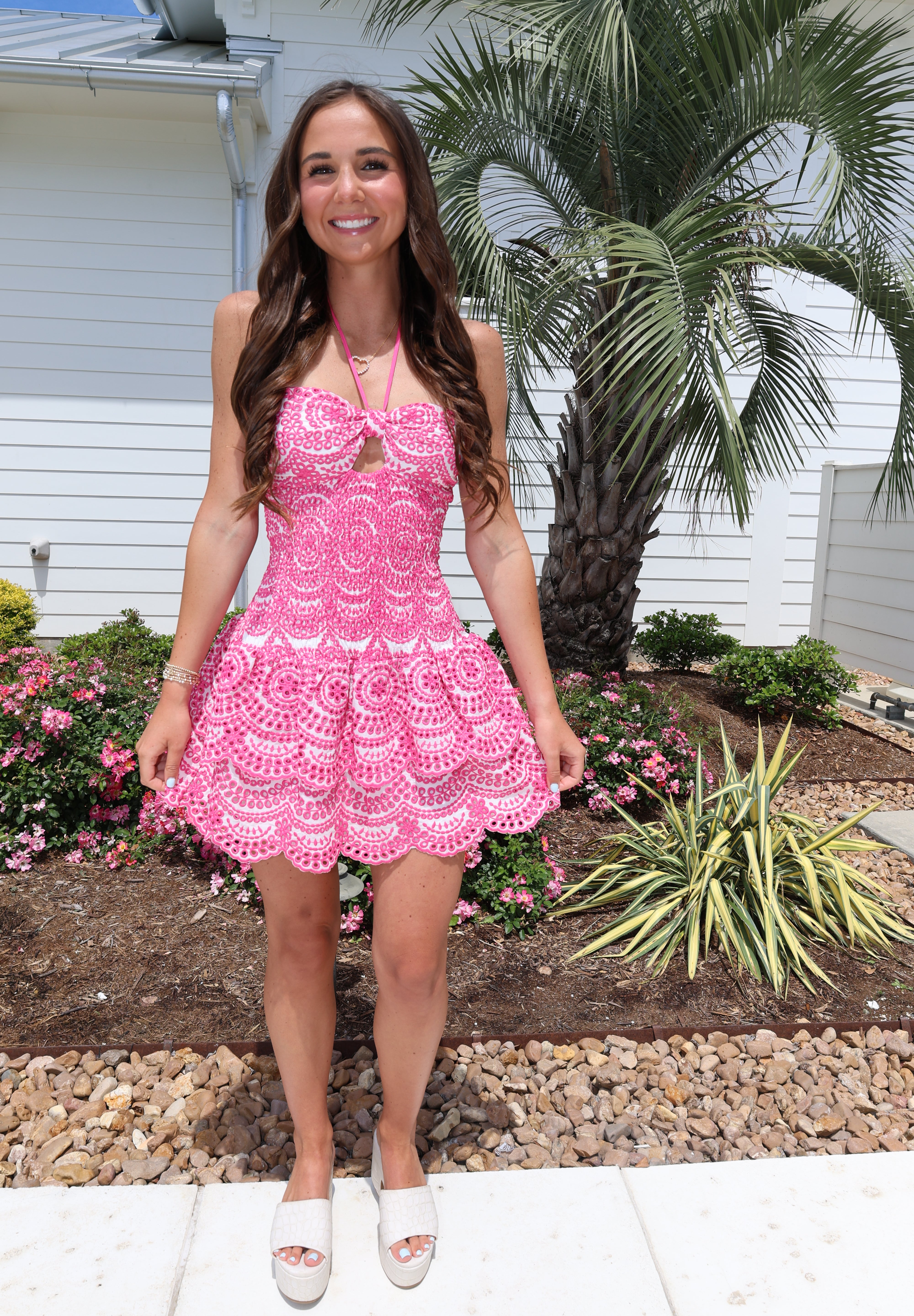 Woman in a pink dress standing outdoors with plants and a house in the background
