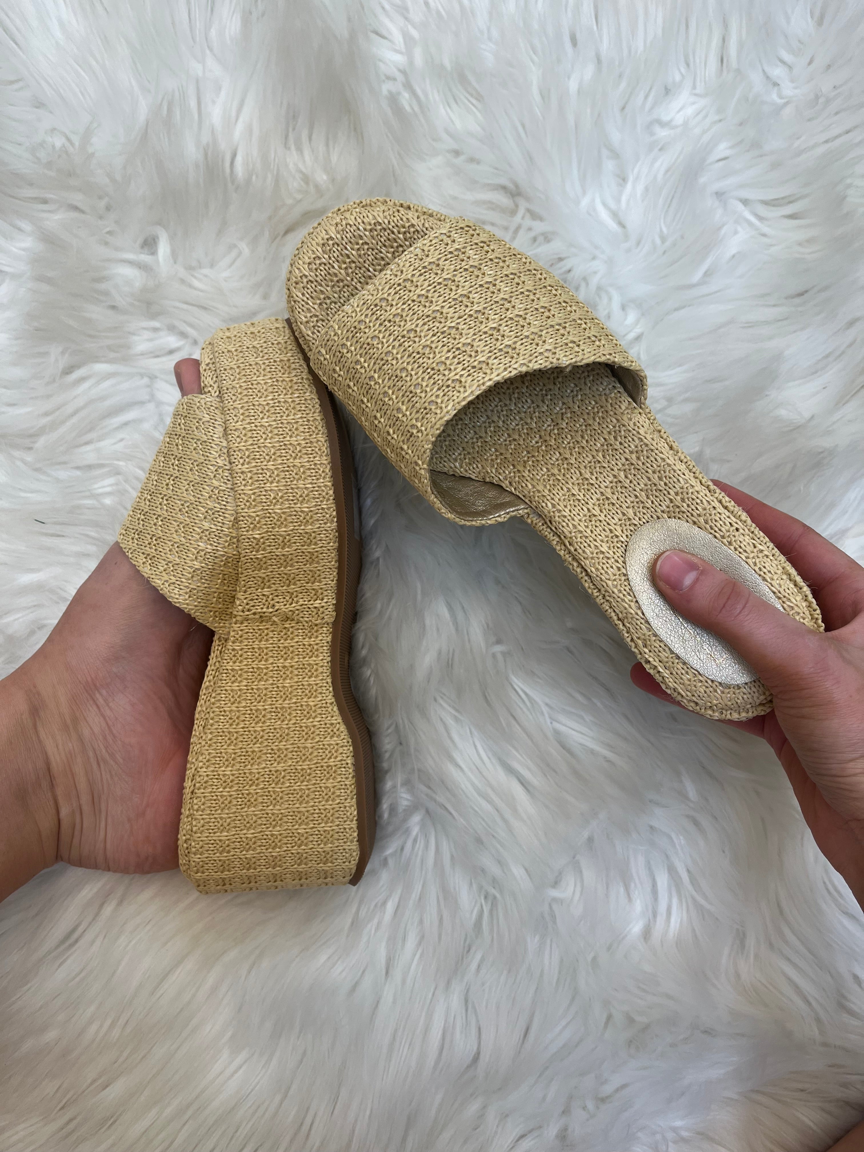 Beige sandal held by a hand on a white fluffy surface