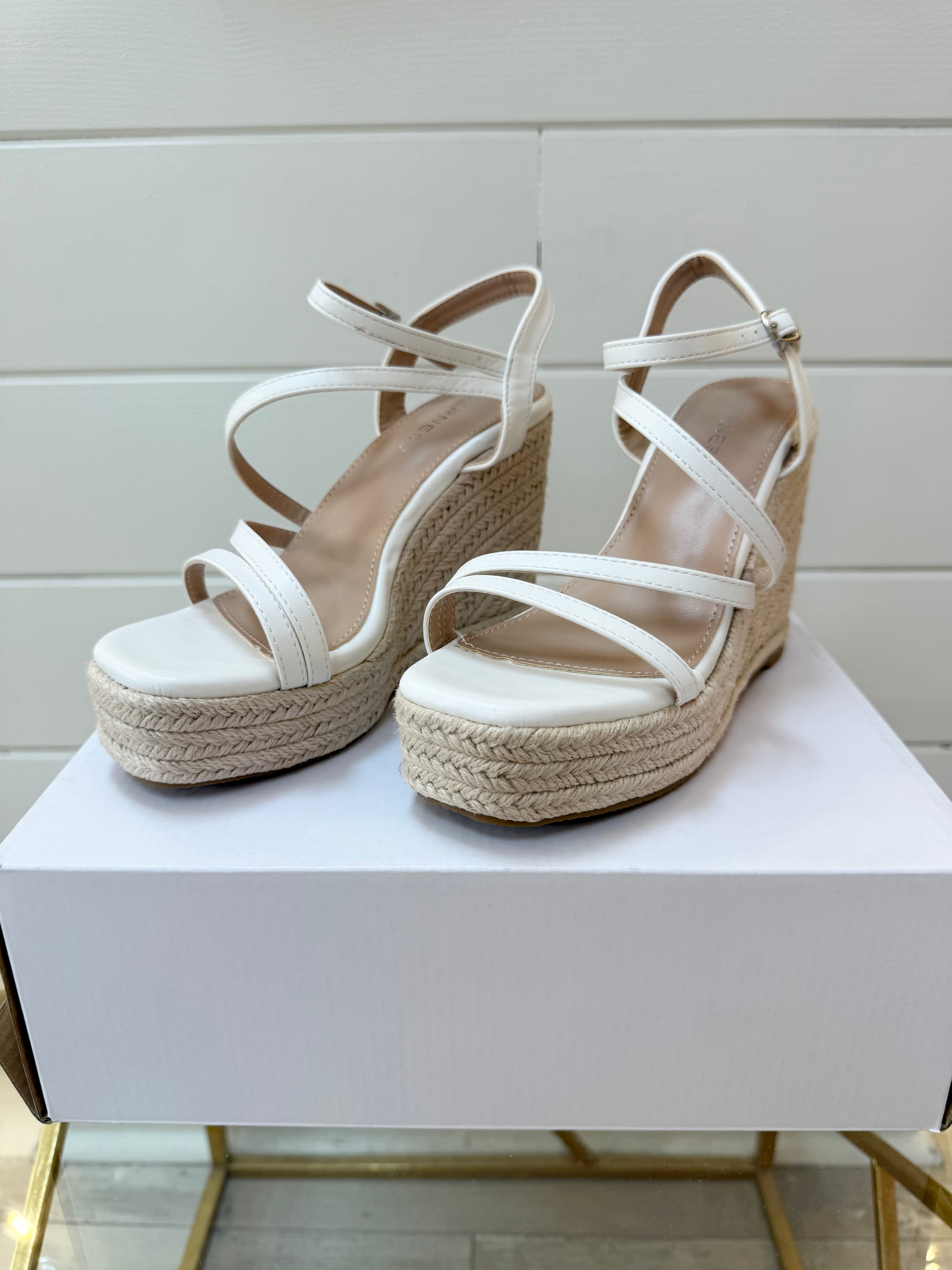 White wedge sandals with espadrille sole on a white surface