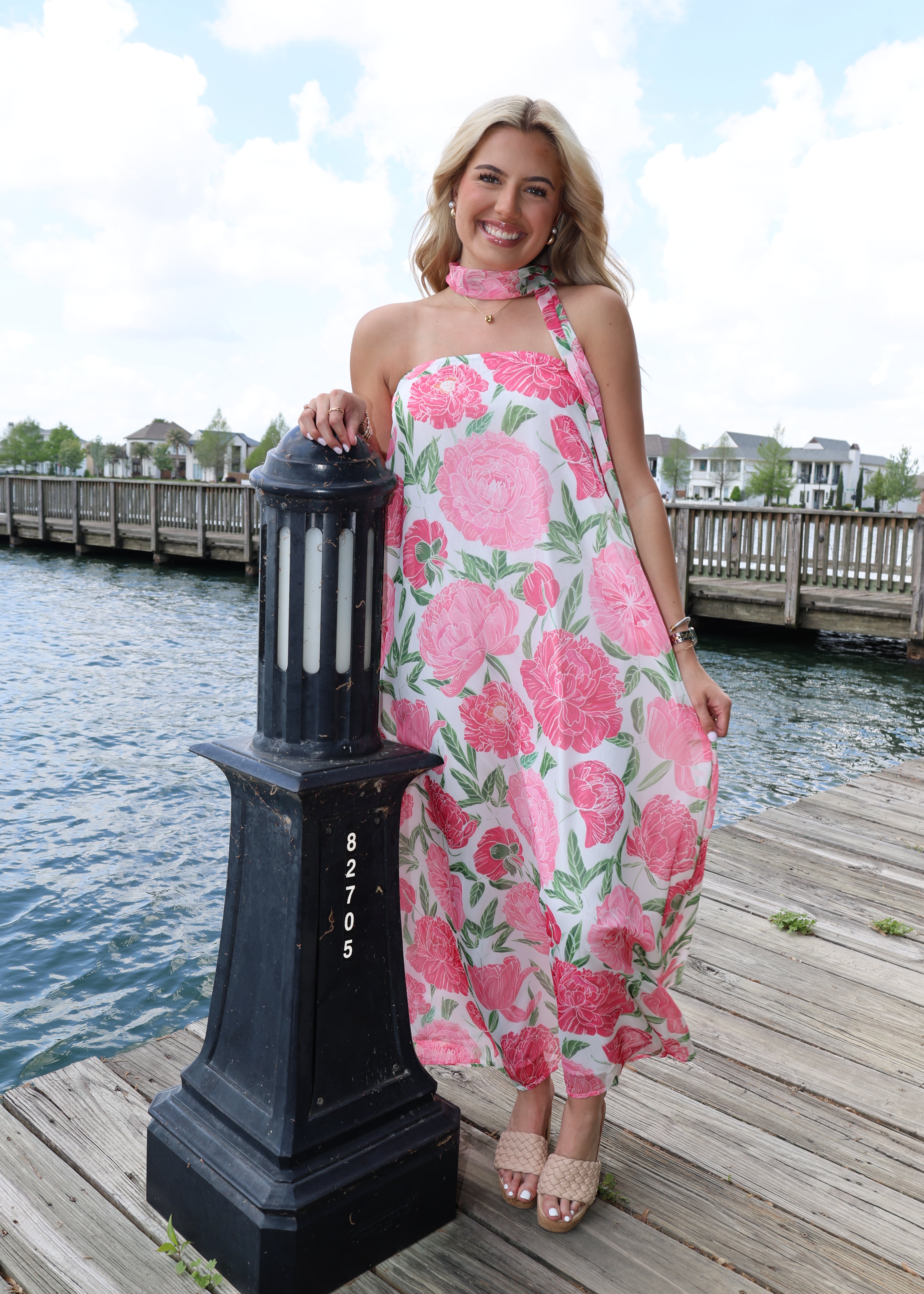Woman in a floral dress holding a black box with 'Gucci' branding by a waterfront.
