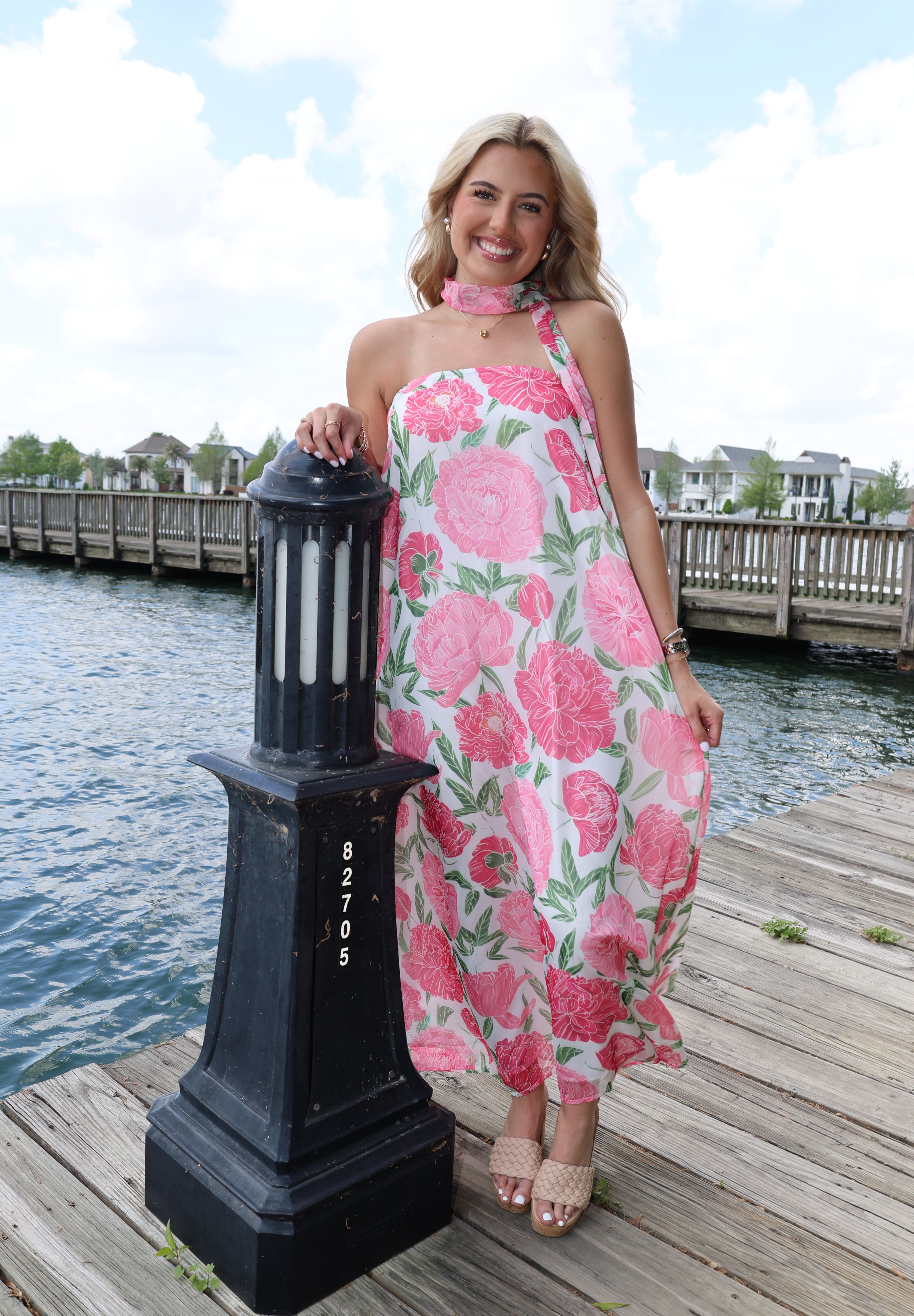 Woman in a floral dress holding a black box with 'Gucci' branding by a waterfront.