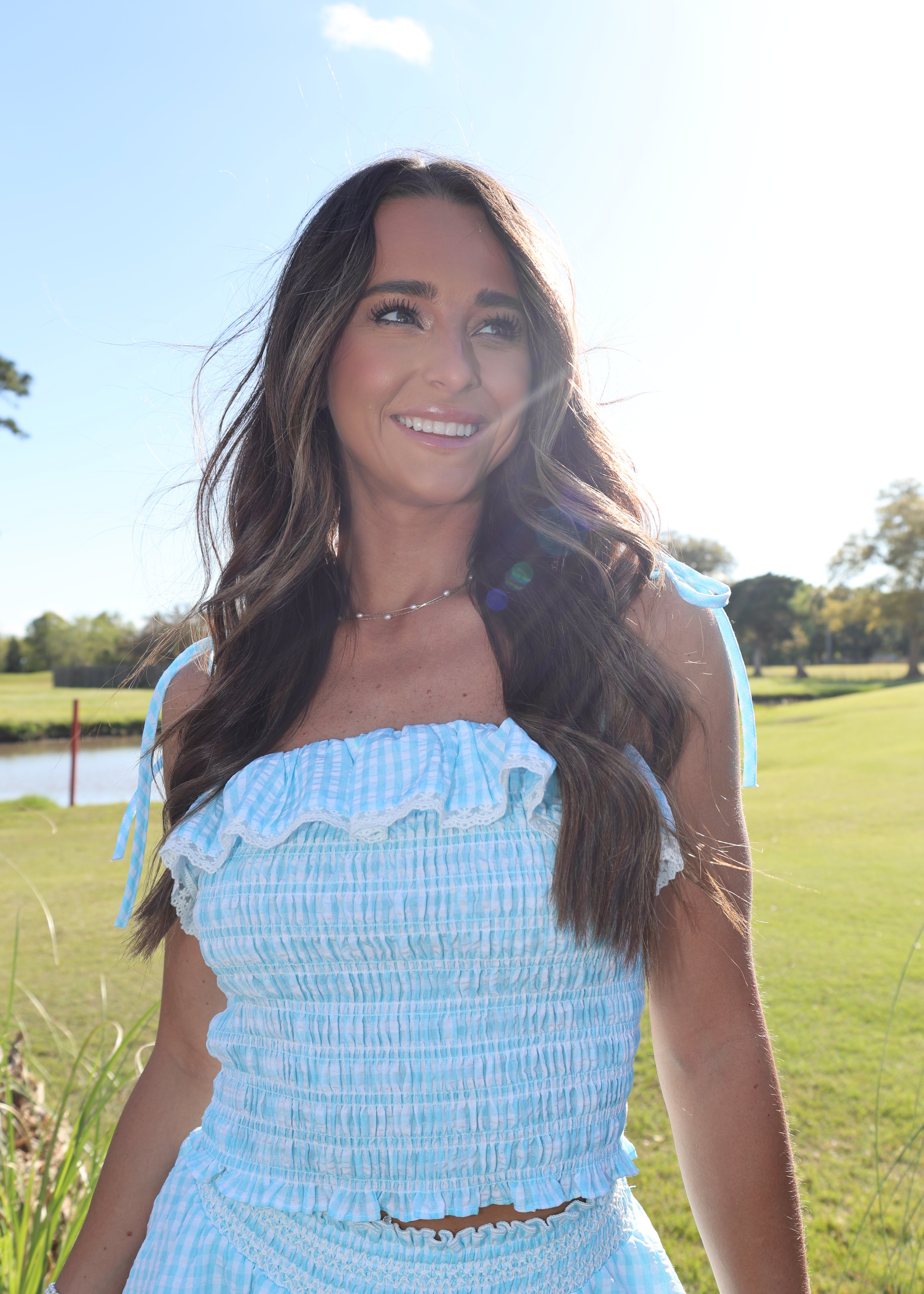 Woman in a light blue dress standing in a grassy field with trees in the background