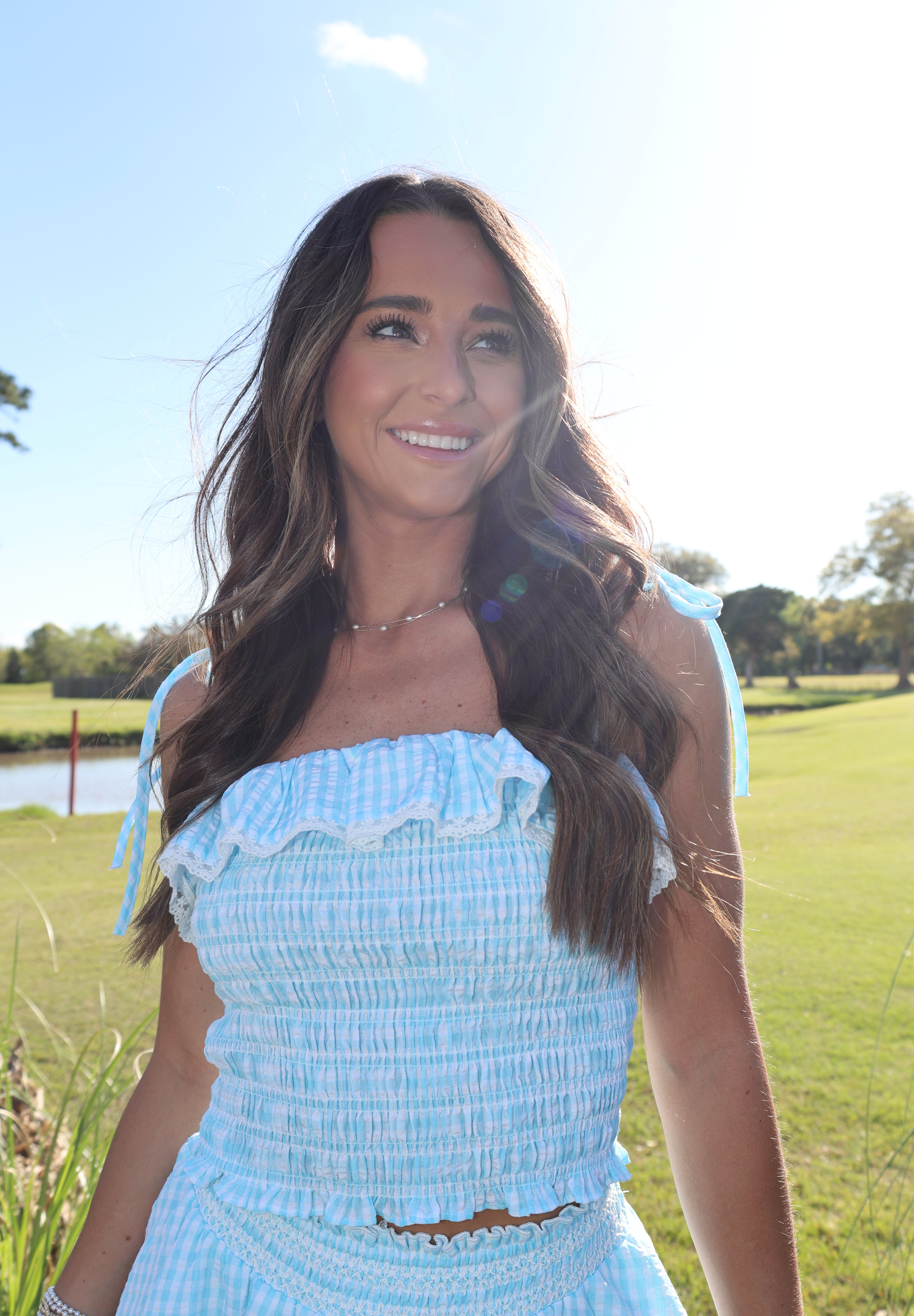 Woman in a light blue dress standing in a grassy field with trees in the background