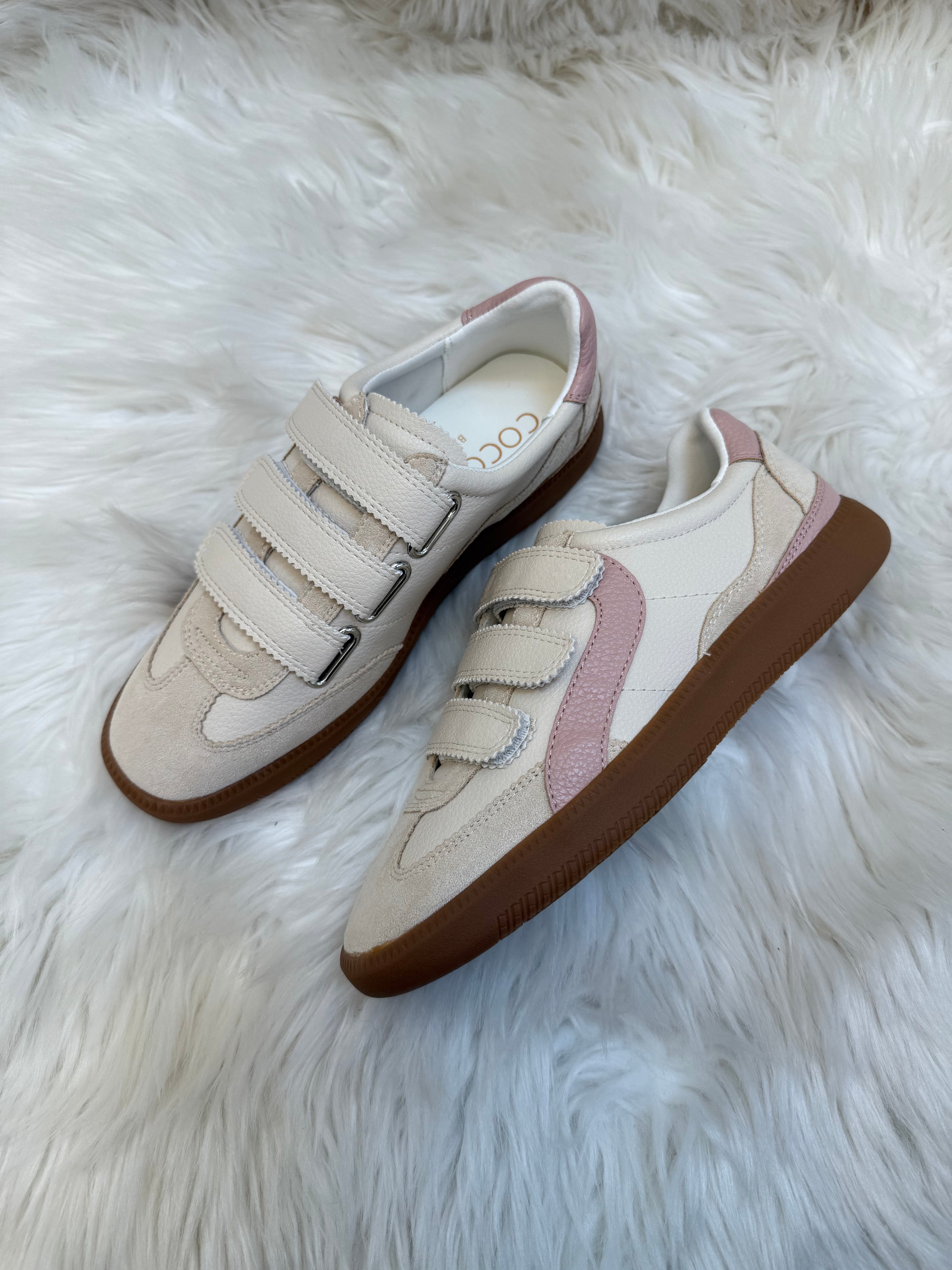 Pair of white sneakers with brown soles on a fluffy white surface