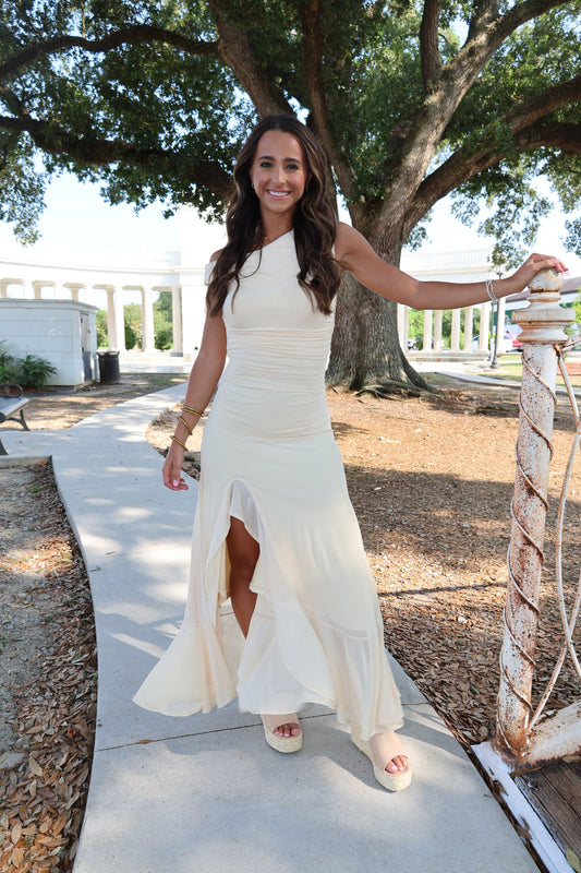 Woman in a white dress standing outdoors with trees and a building in the background