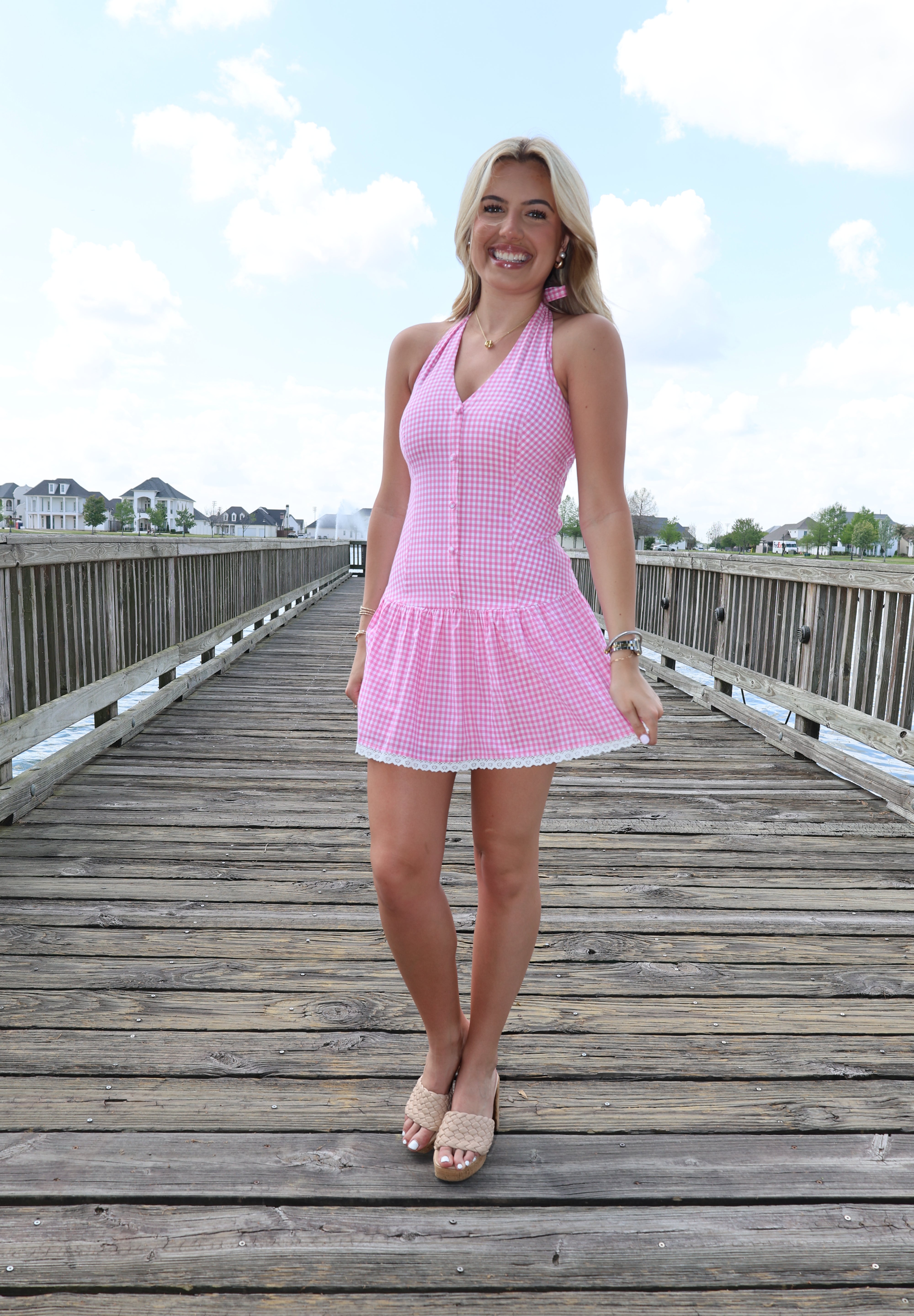 Woman in a pink dress standing on a wooden boardwalk with a clear sky.