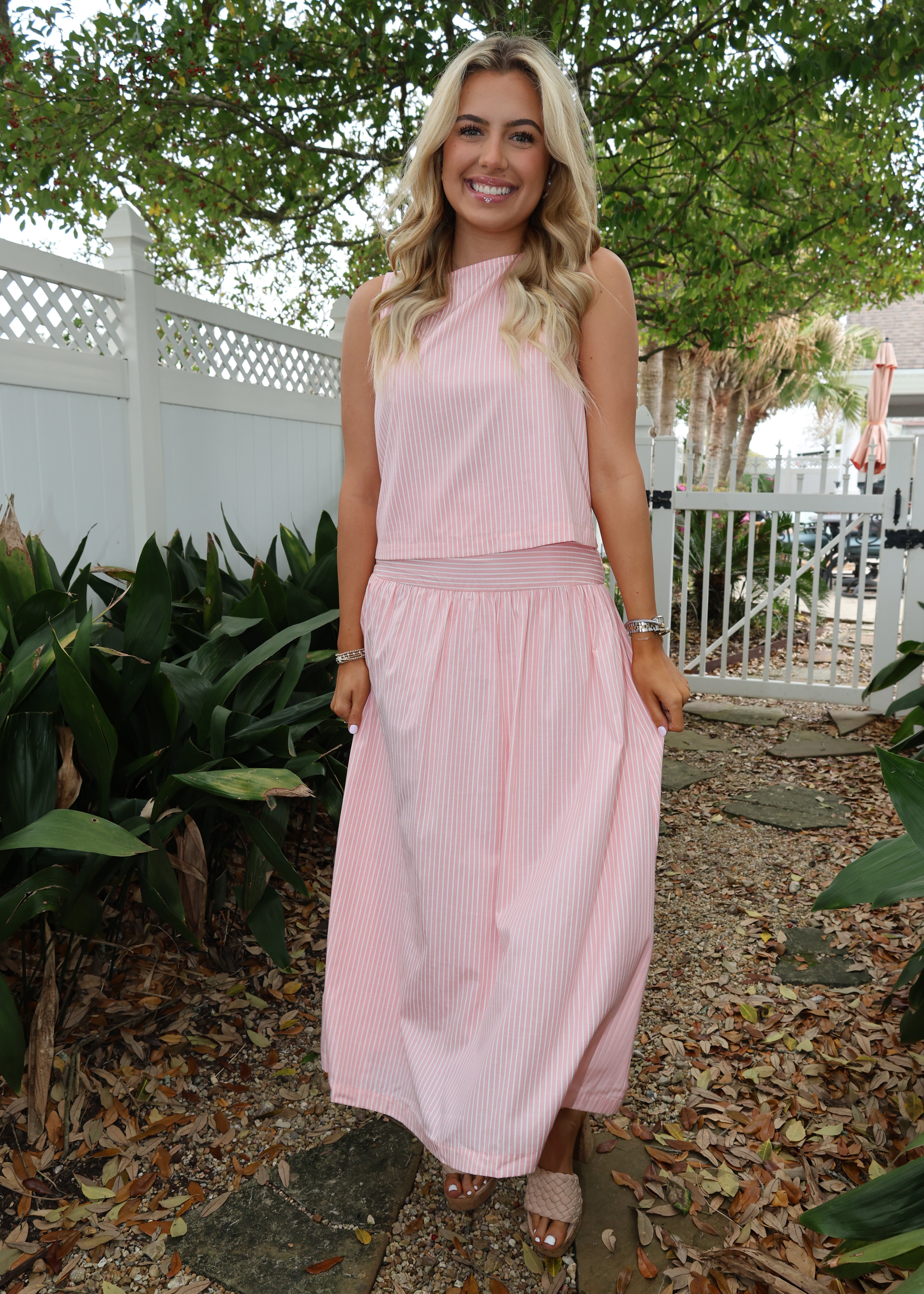 Woman in a pink dress standing outdoors with greenery around