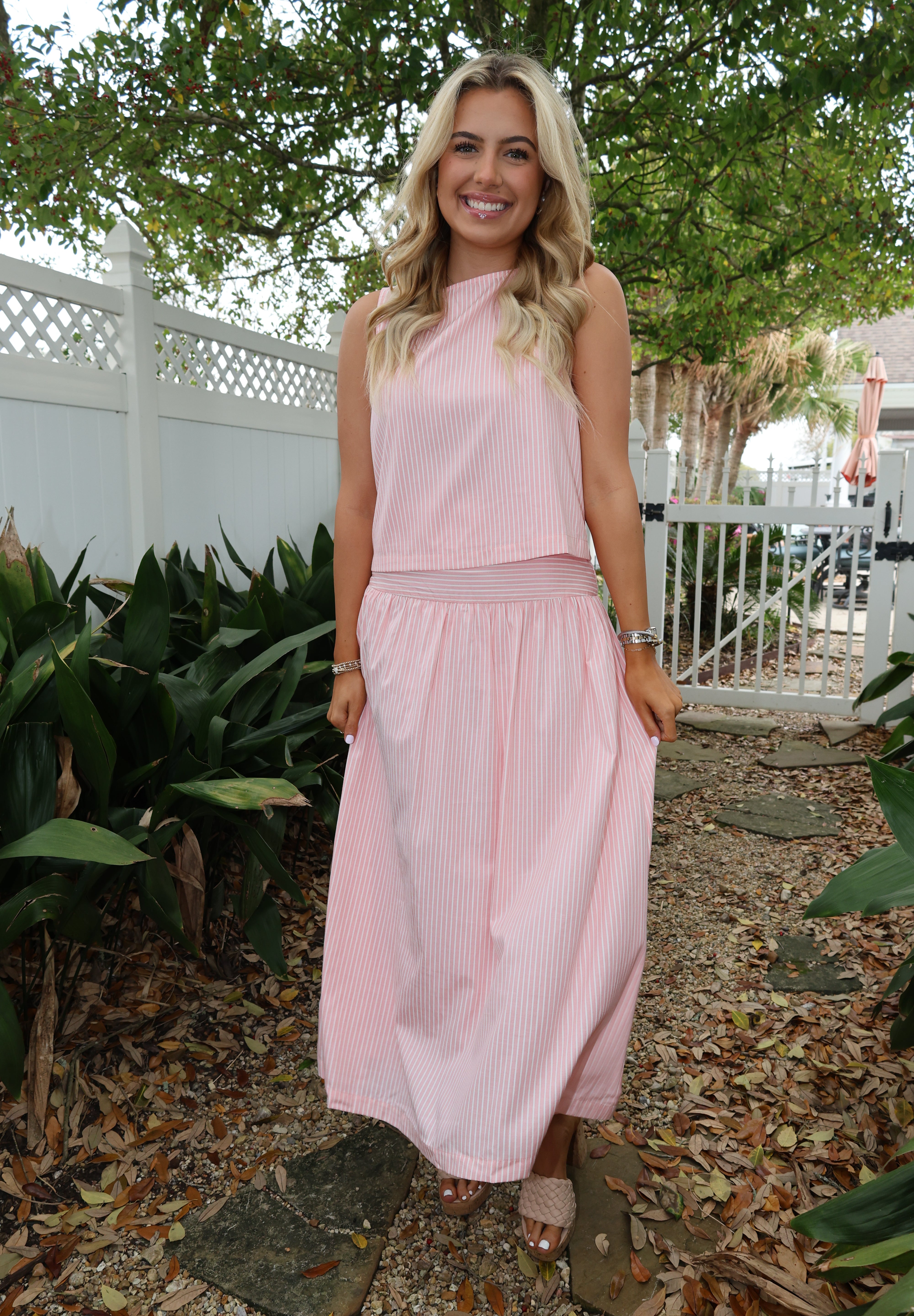 Woman in a pink dress standing outdoors with greenery around