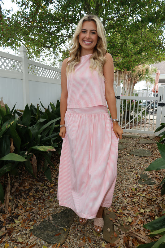 Woman in a pink dress standing outdoors with greenery around